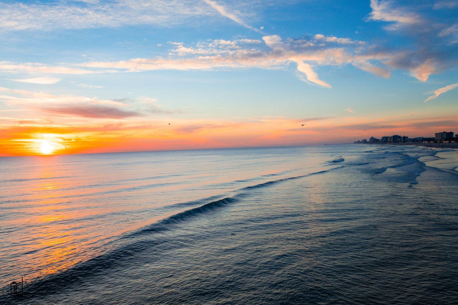 Dramatic sunset over ocean horizon with golden sun reflecting on calm waters and silhouetted coastline in distance.