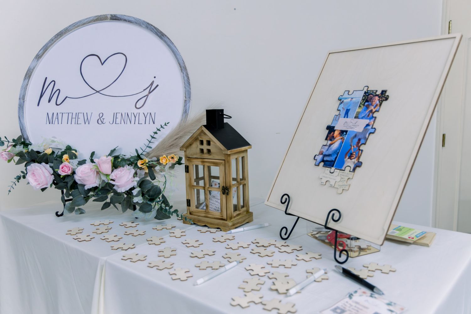 Wedding guest book table with puzzle pieces, floral hoop sign reading Matthew & Jennylyn, lantern centerpiece, and framed photo display.