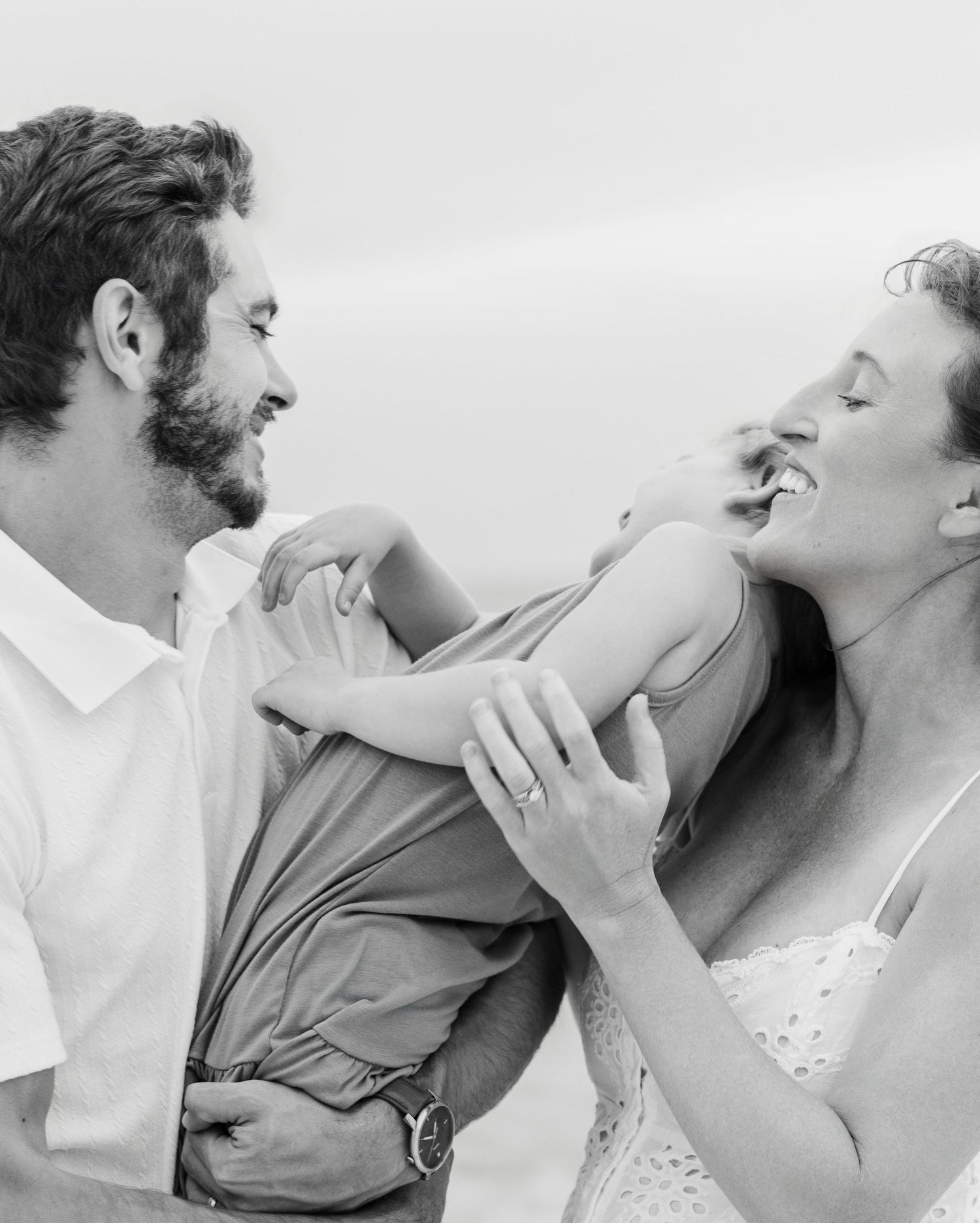 Black and white photo of a laughing couple embracing outdoors, woman wearing an engagement ring on her hand.