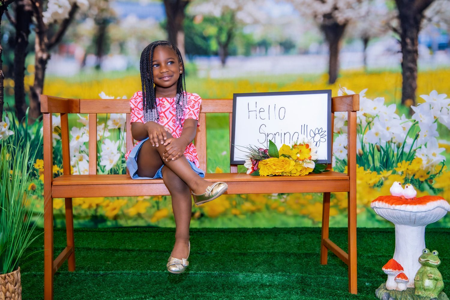 A person sits on a wooden bench outdoors holding a sign while surrounded by lush greenery and flowers.