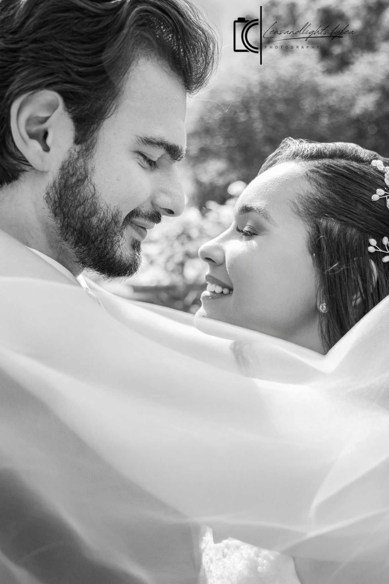 Black and white wedding photo of a smiling bride and groom sharing a romantic moment, with veil flowing around them.