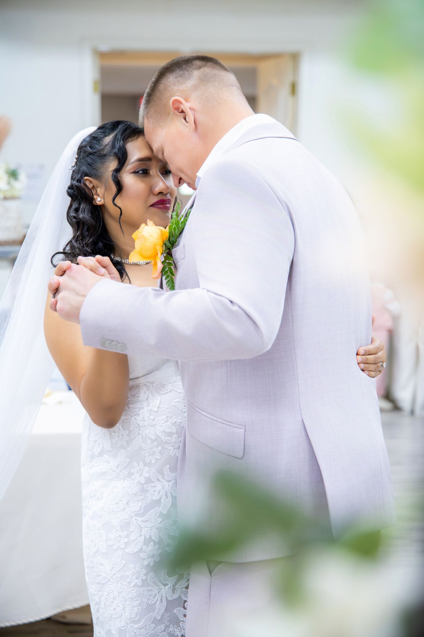 Bride and groom share an intimate first dance, with the bride in a white lace gown and groom in a light gray suit.