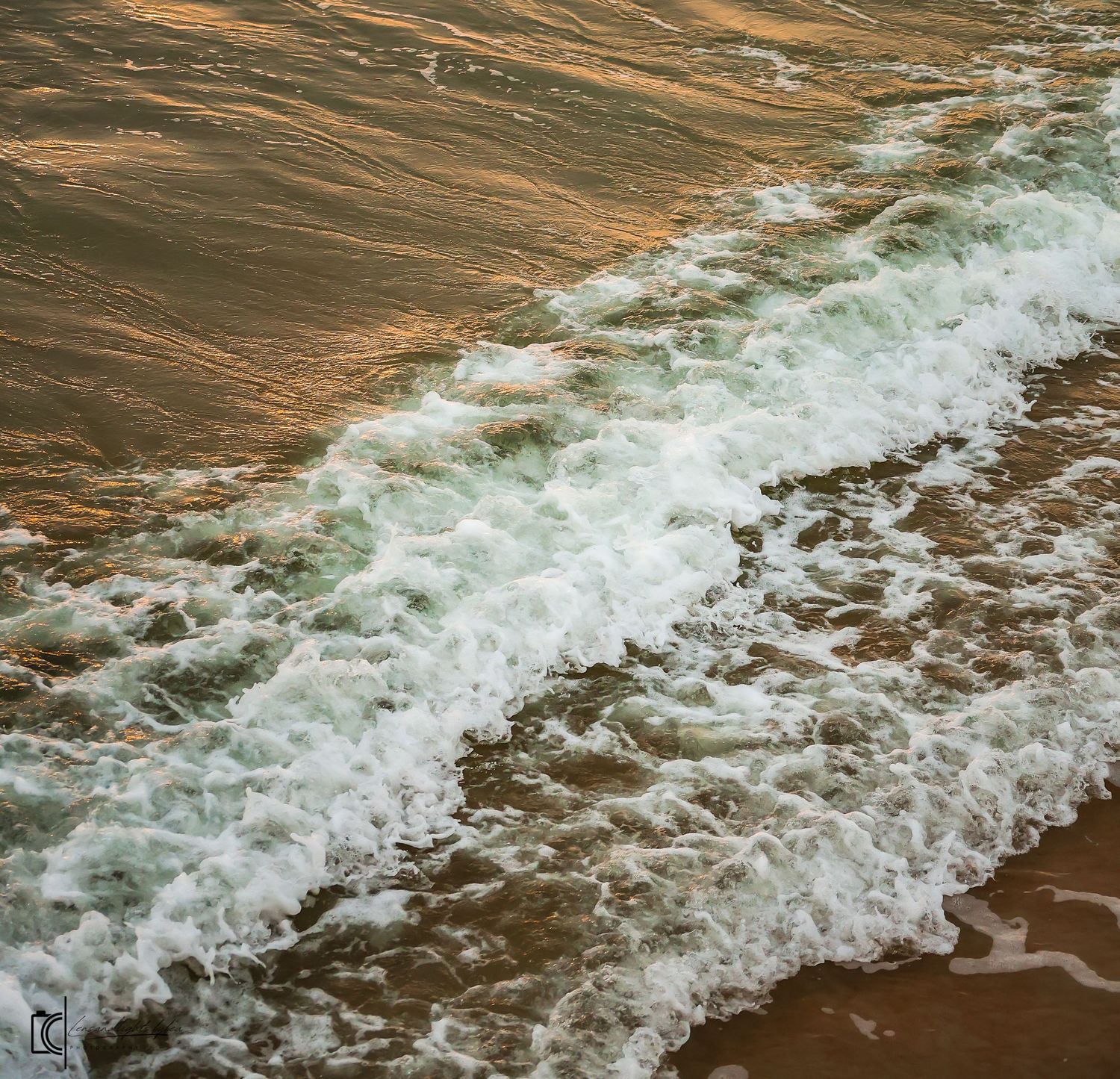 Aerial view of ocean waves crashing onto a sandy beach with turquoise water creating white foam patterns.