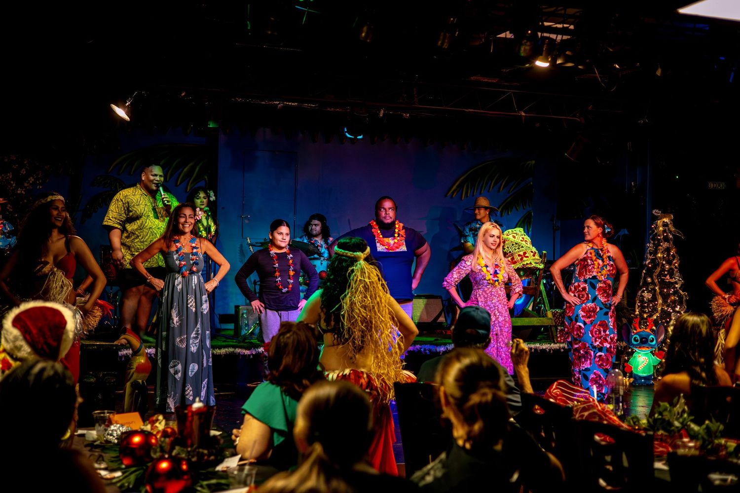Performers in colorful costumes dance on a dark stage with vibrant lighting during a theatrical show.