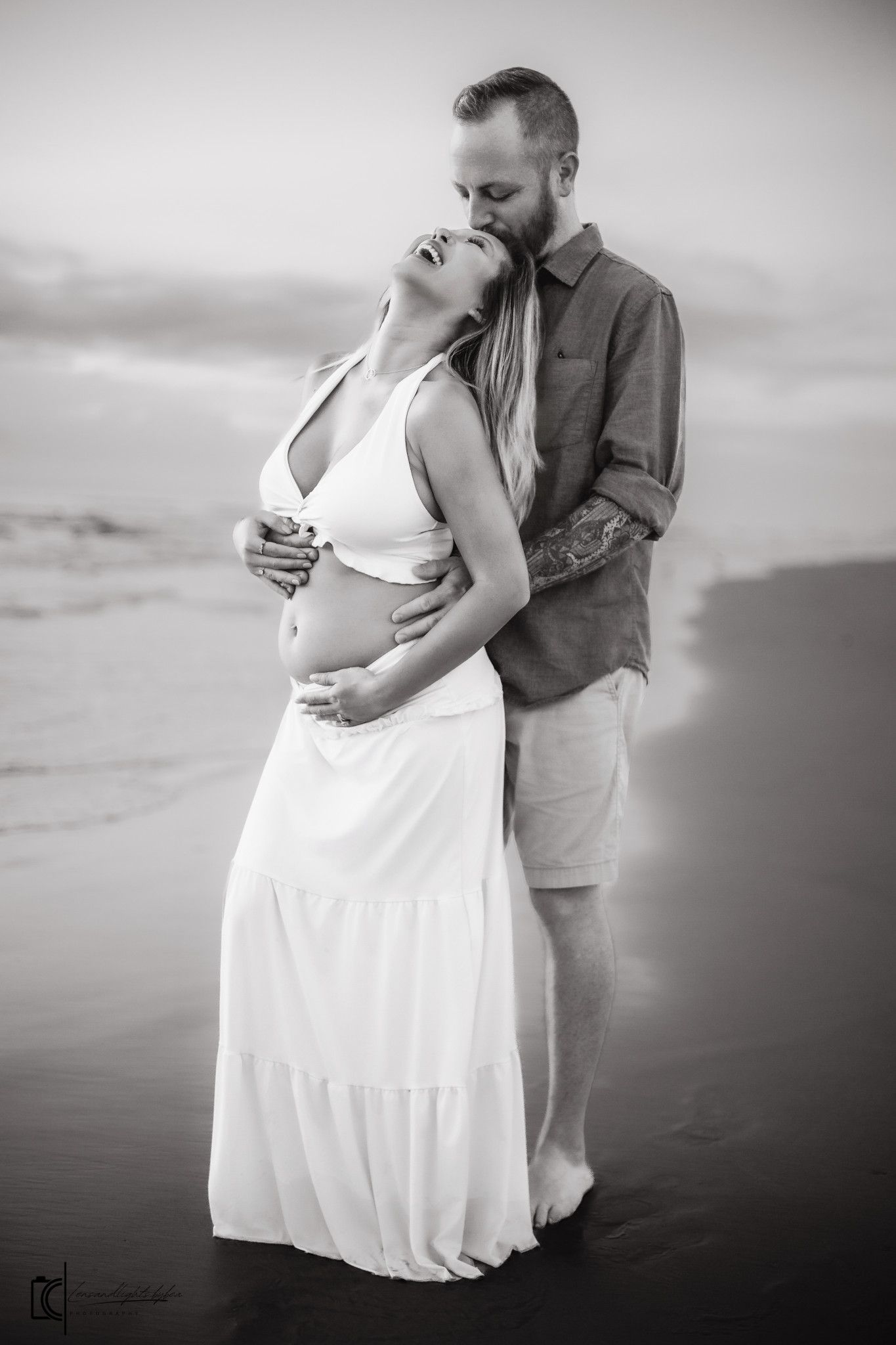 Black and white maternity photoshoot series showing couple embracing on beach at sunset with flowing white dress.