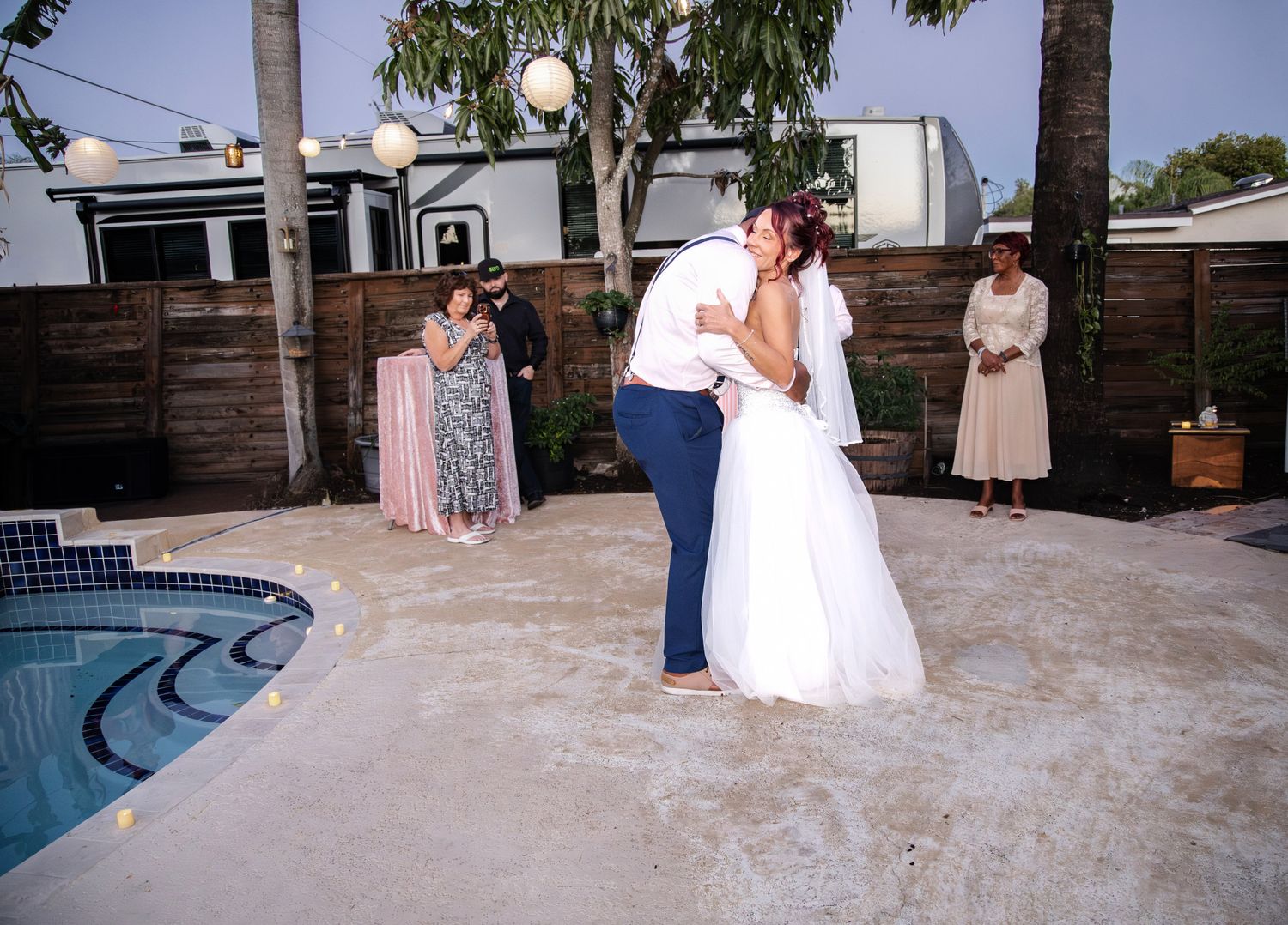A couple shares their first dance as newlyweds beside a pool during an intimate backyard wedding celebration.