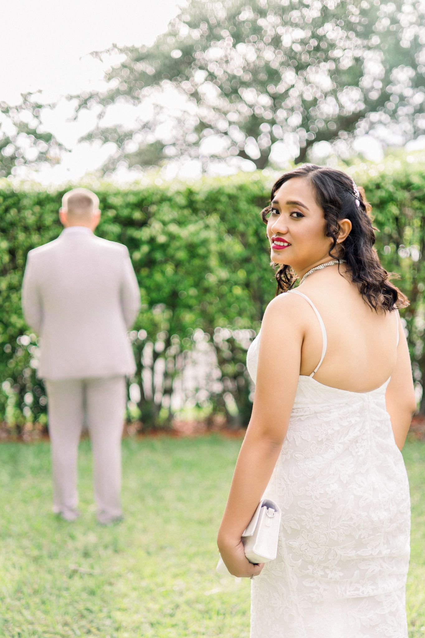 Bride in white gown smiling over shoulder at groom during outdoor first look wedding moment.