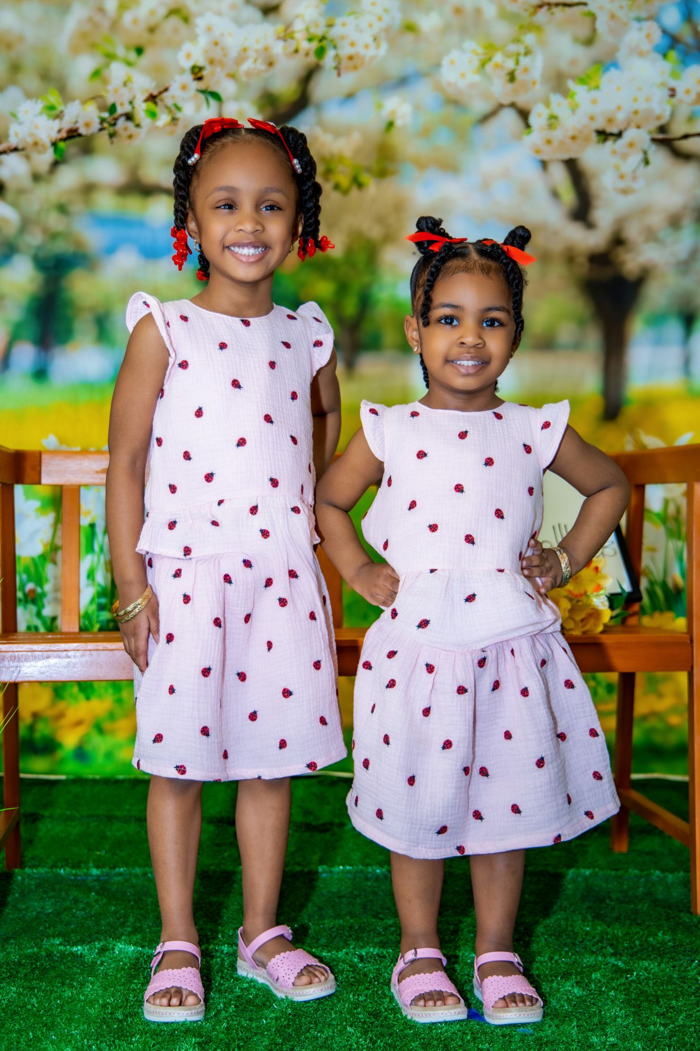 Two matching white dresses with red heart patterns on green grass in a sunny garden setting.