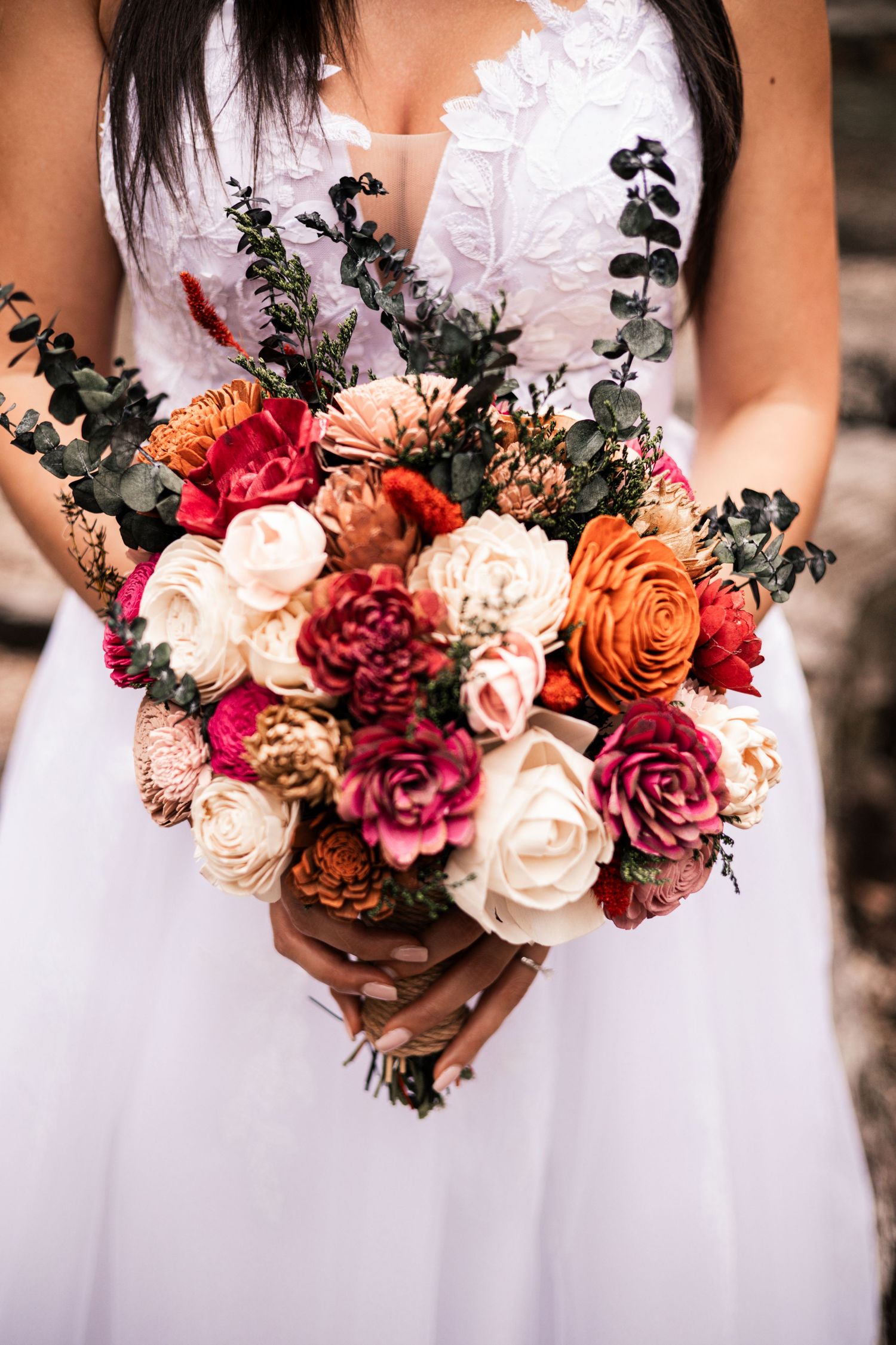 A row of wedding bouquets featuring burgundy, orange, and cream roses with dark greenery against white dresses.