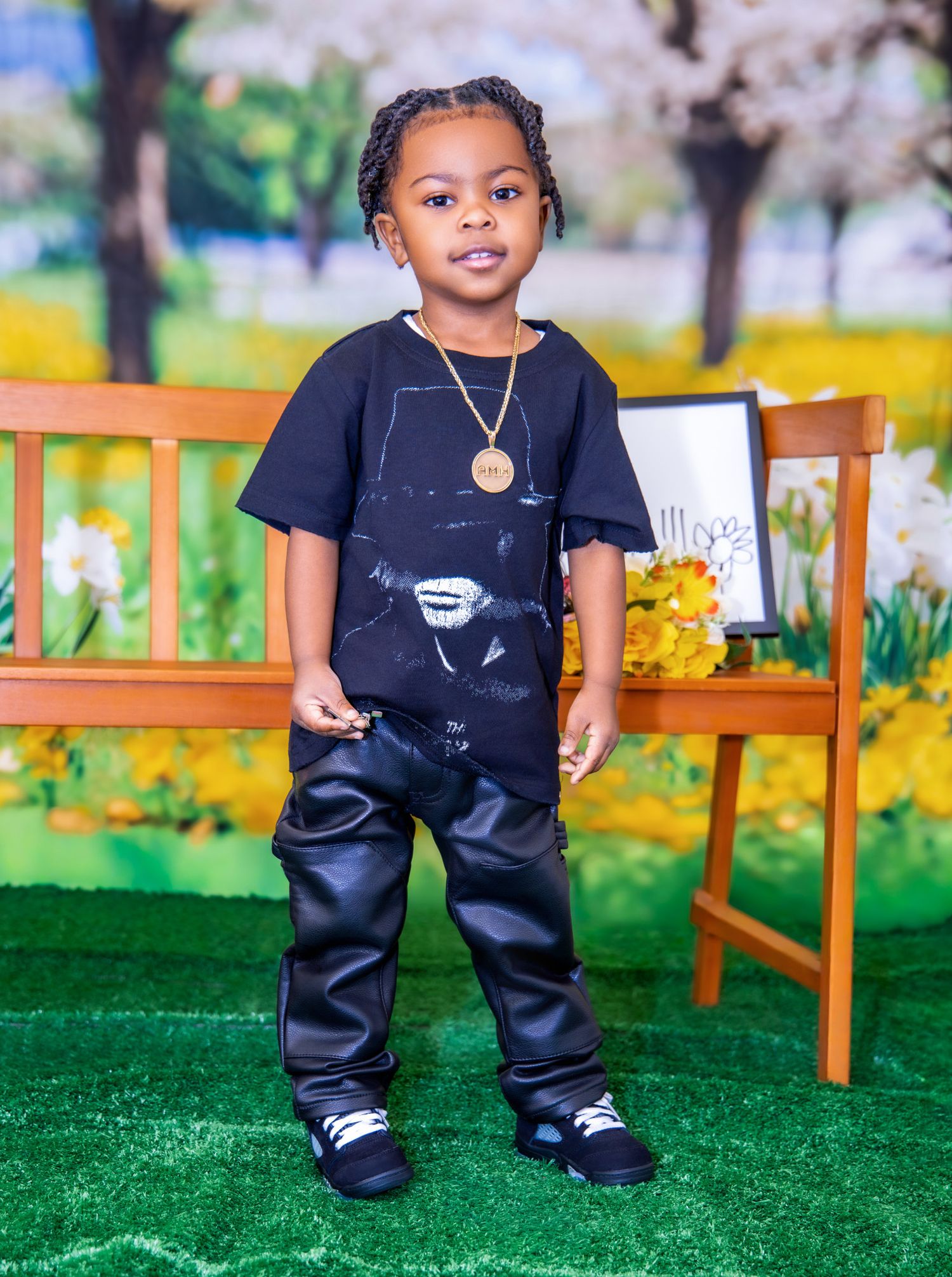 Small child wearing dark overalls and white shoes stands on artificial grass near orange wooden benches in outdoor setting.