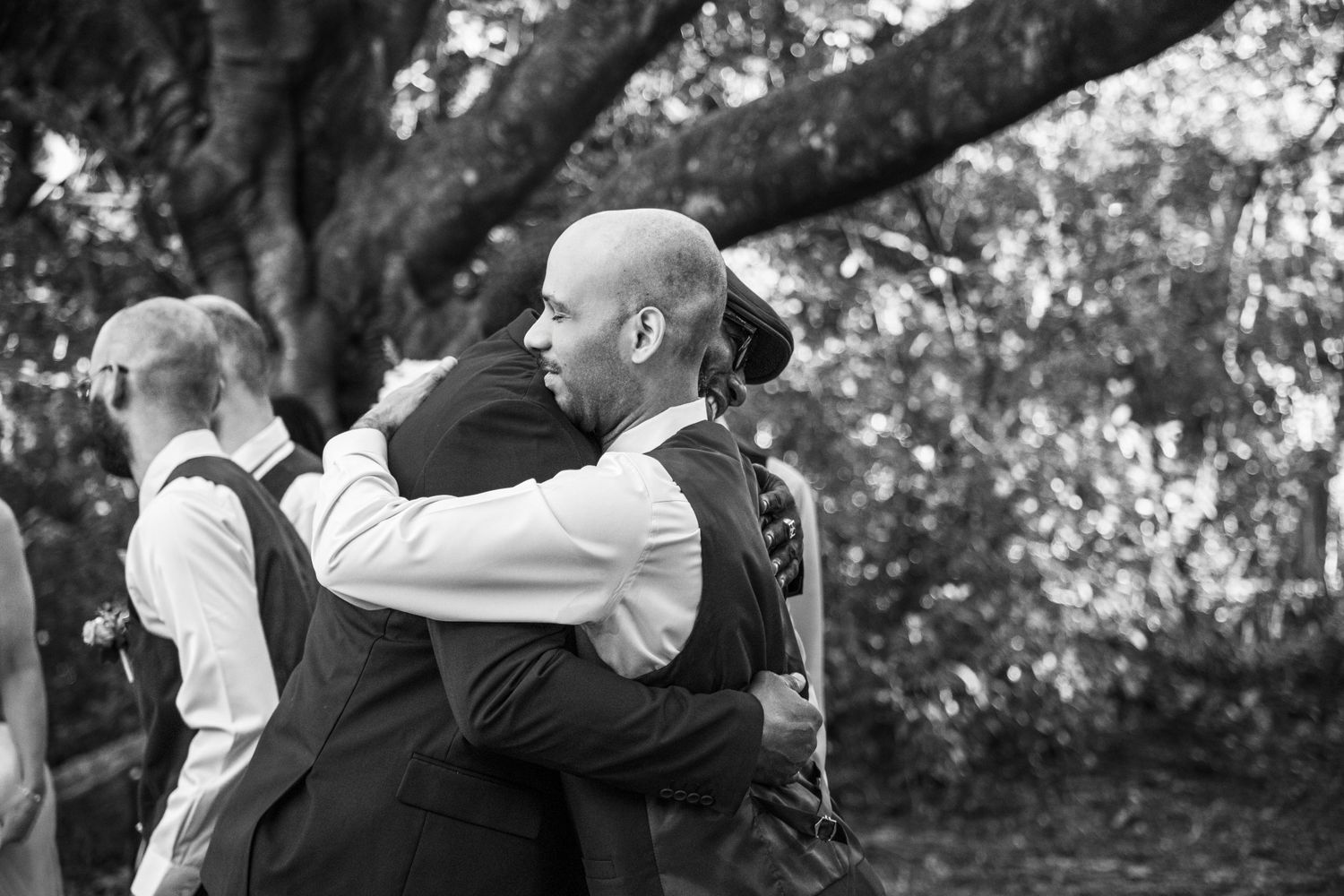 A couple in formal wedding attire embrace and kiss while standing in a scenic outdoor garden setting.
