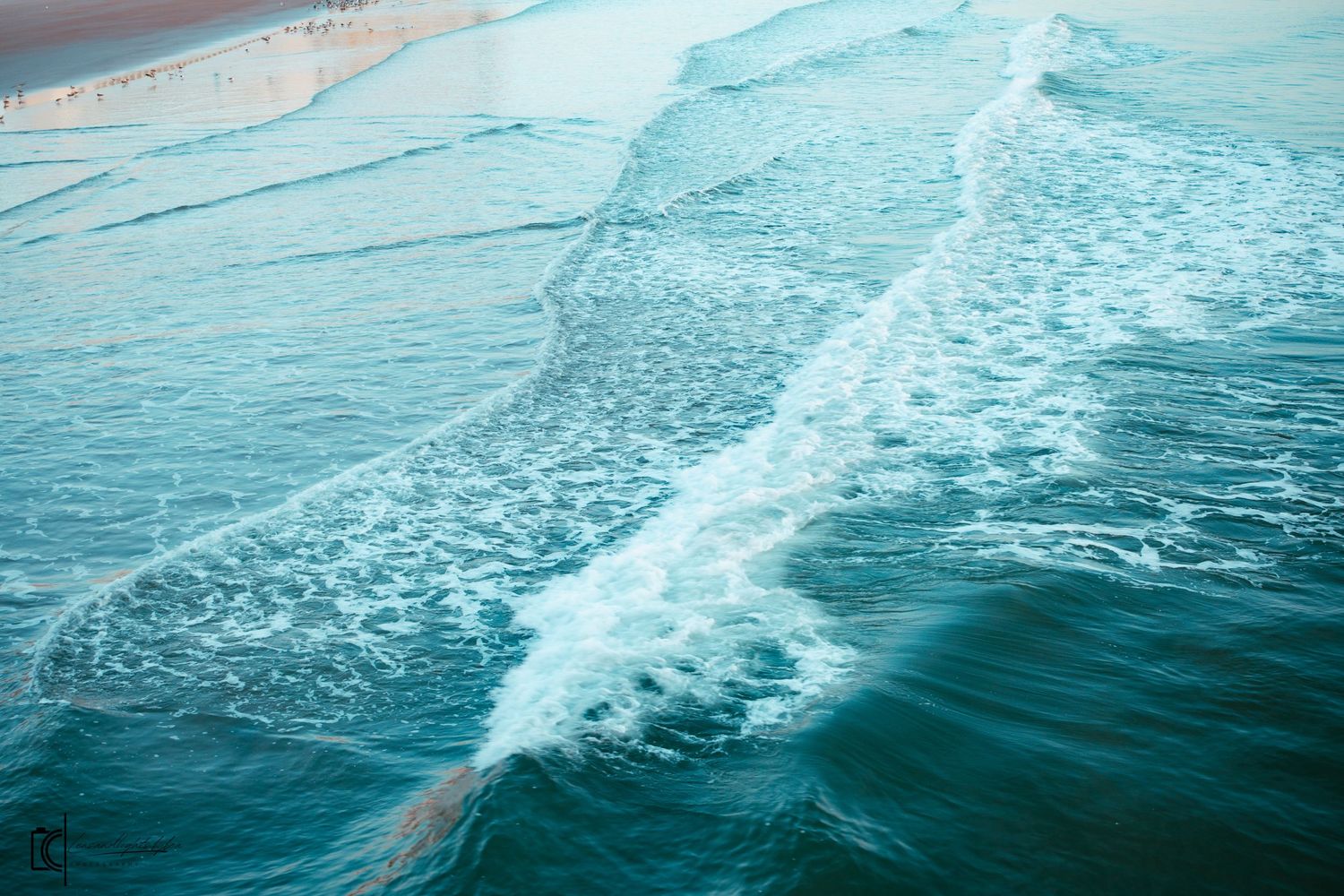 Aerial view of turquoise ocean waves breaking and creating white foam patterns against dark blue water.