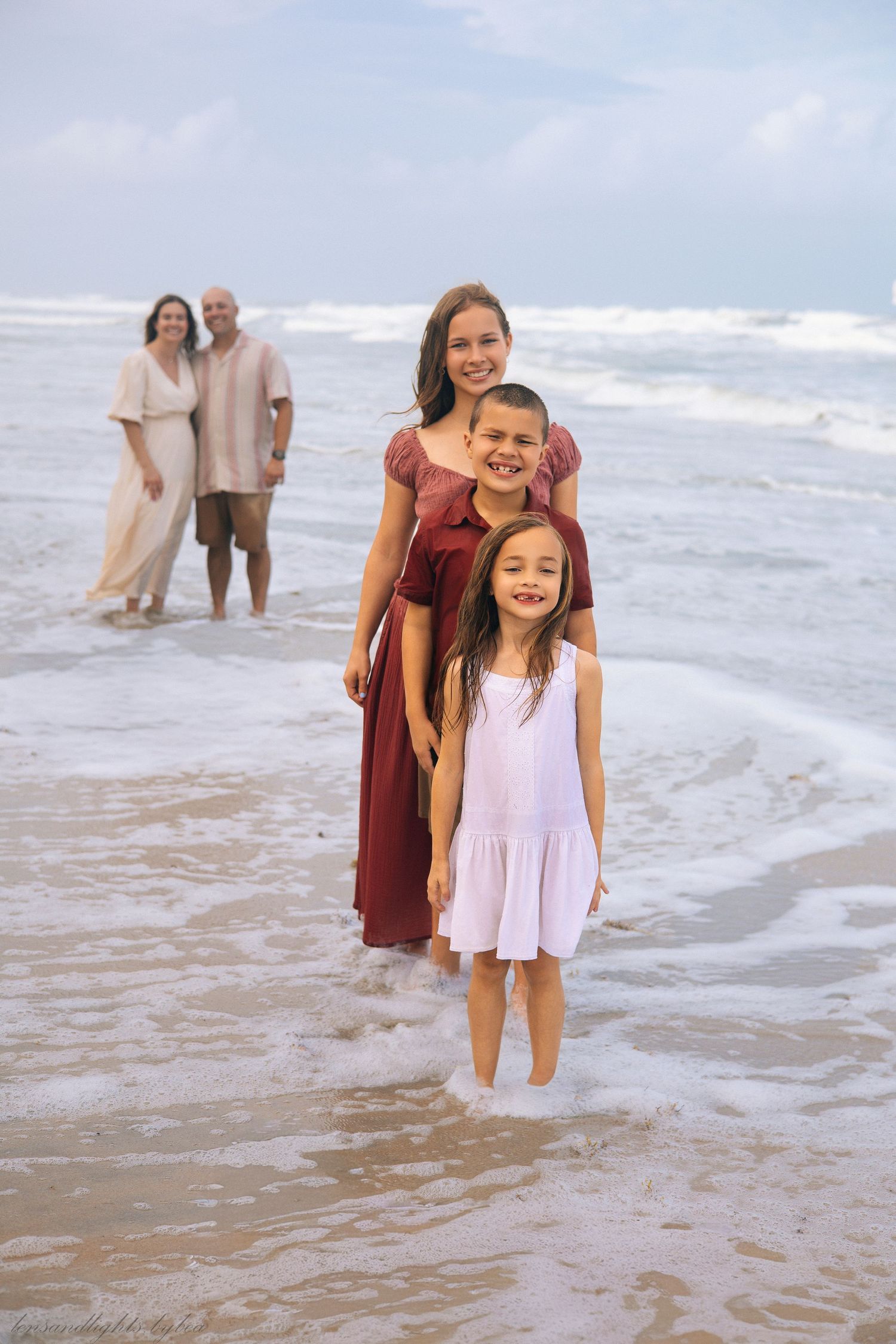 Family members play and laugh together in the ocean waves at the beach.