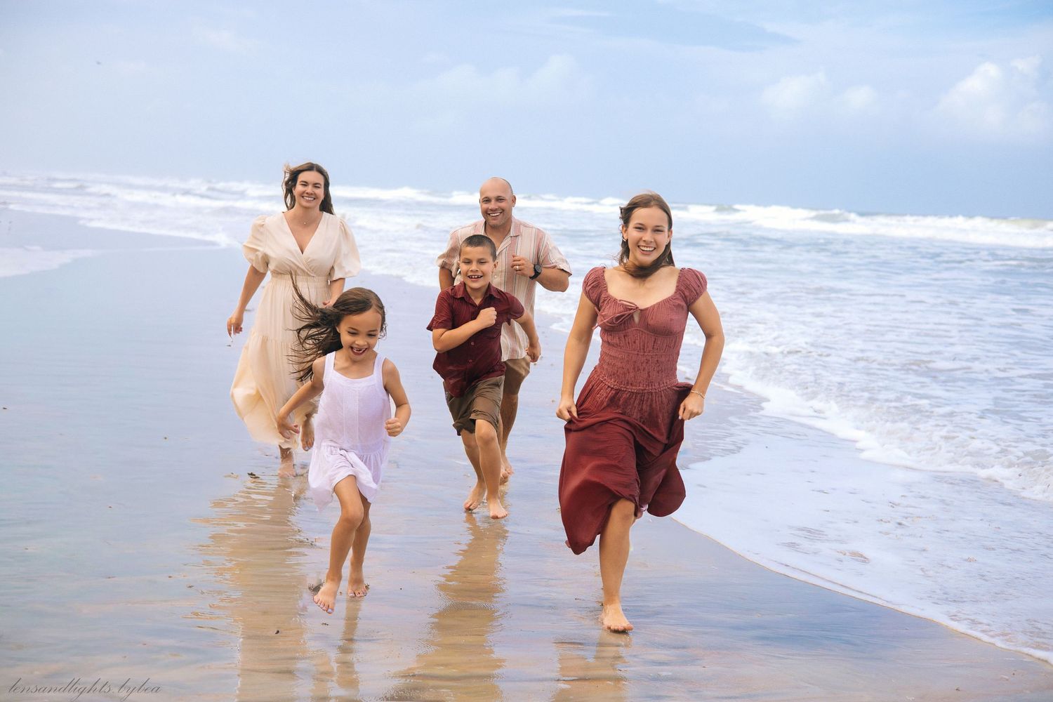 Group running and splashing through shallow ocean water during sunset beach photos.