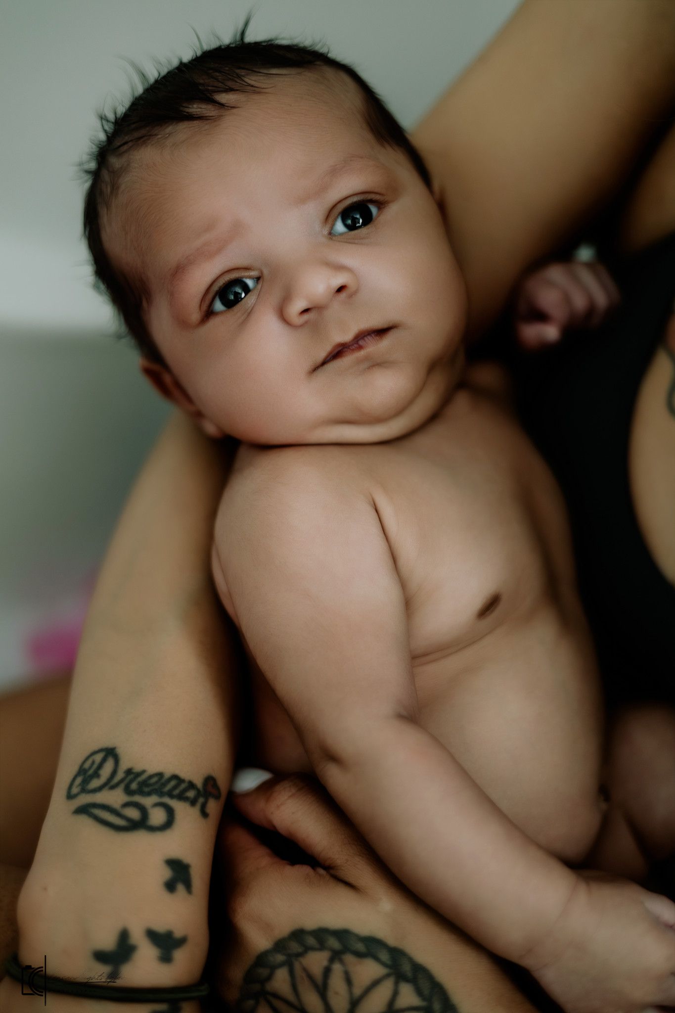 Close-up photos showing a small baby and visible tattoo artwork on what appears to be a parent's arm.
