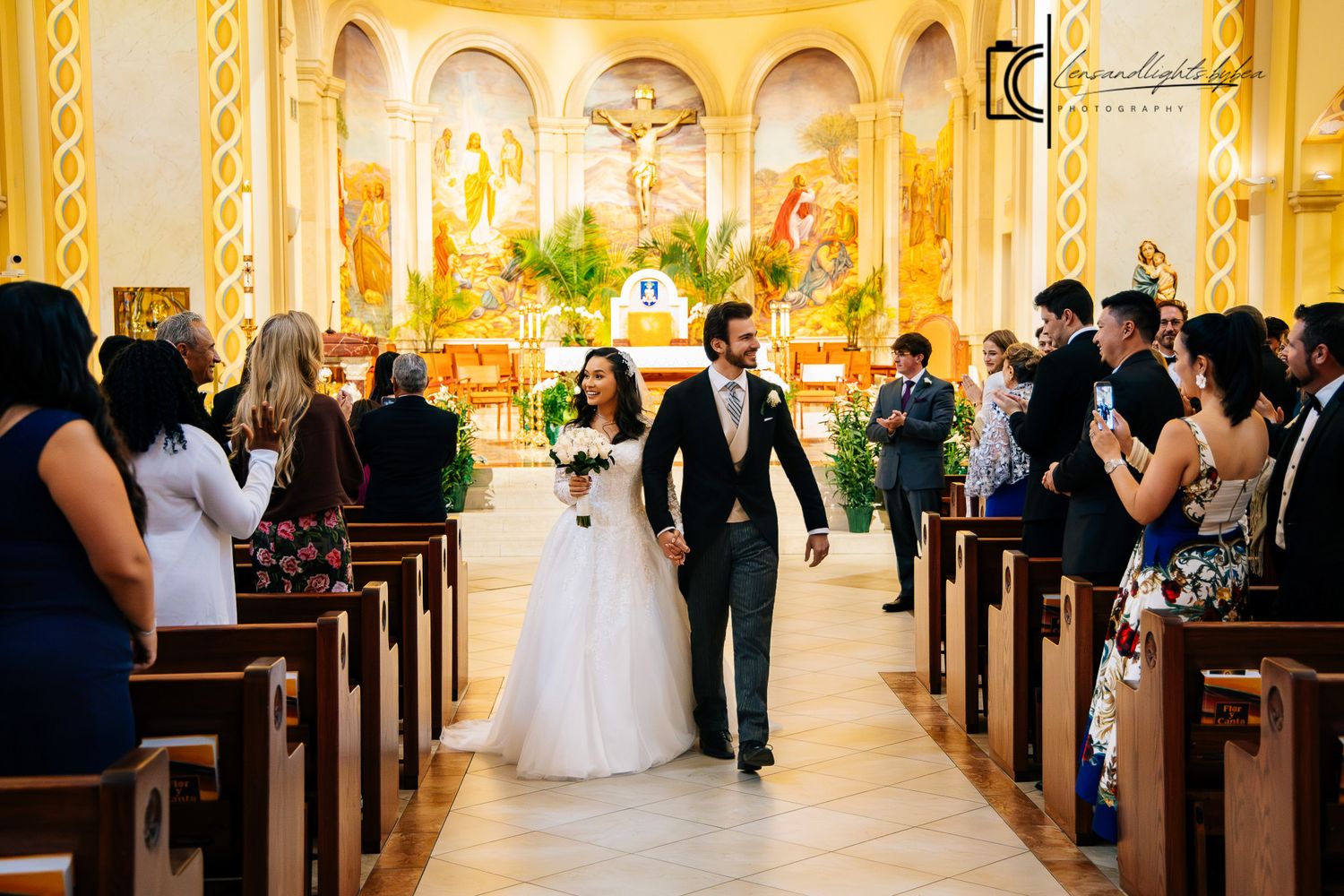 Bride and groom walk down the aisle of a decorated Catholic church after their wedding ceremony.