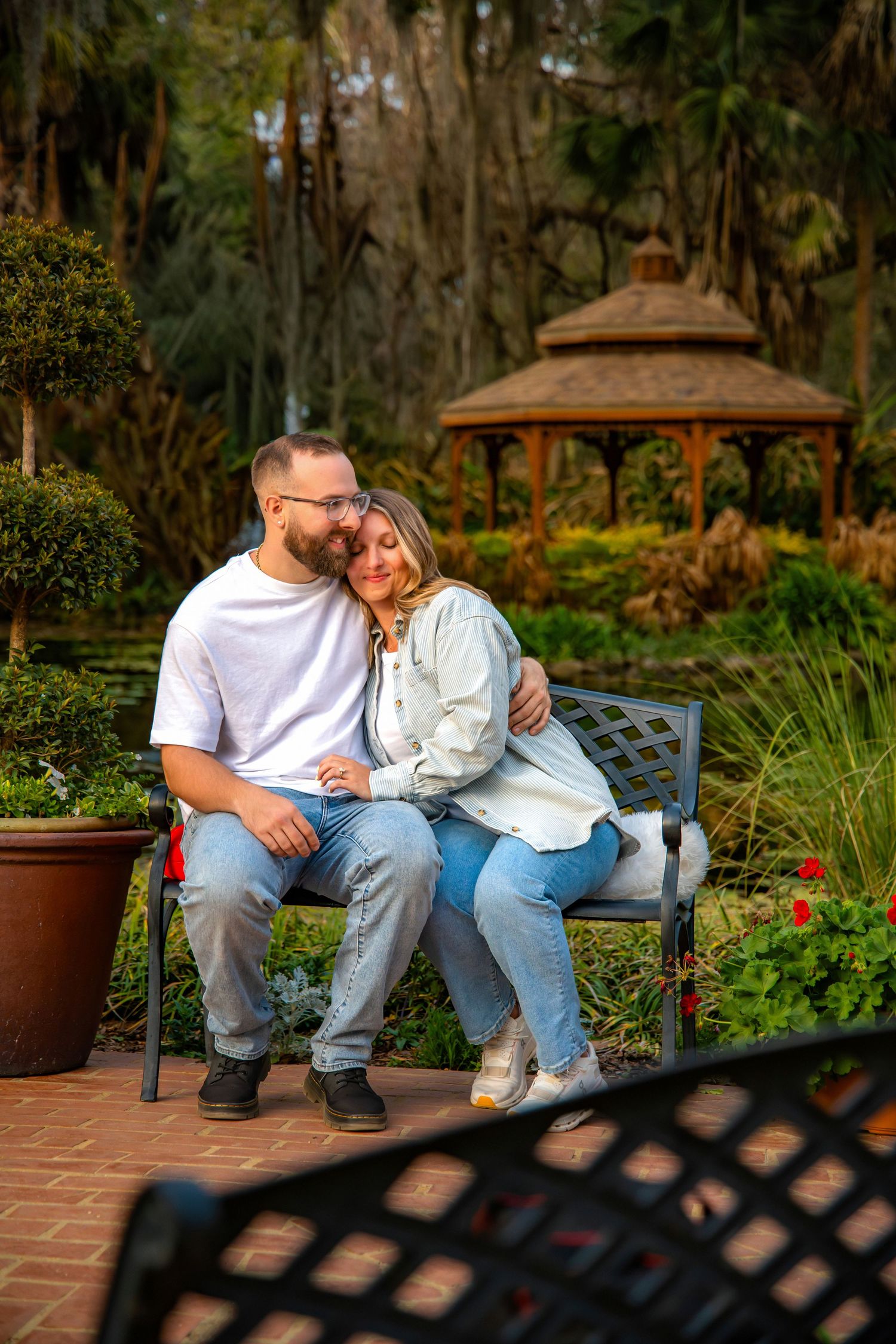 Couple sharing an intimate moment while sitting together on a wooden bench in a lush garden setting.