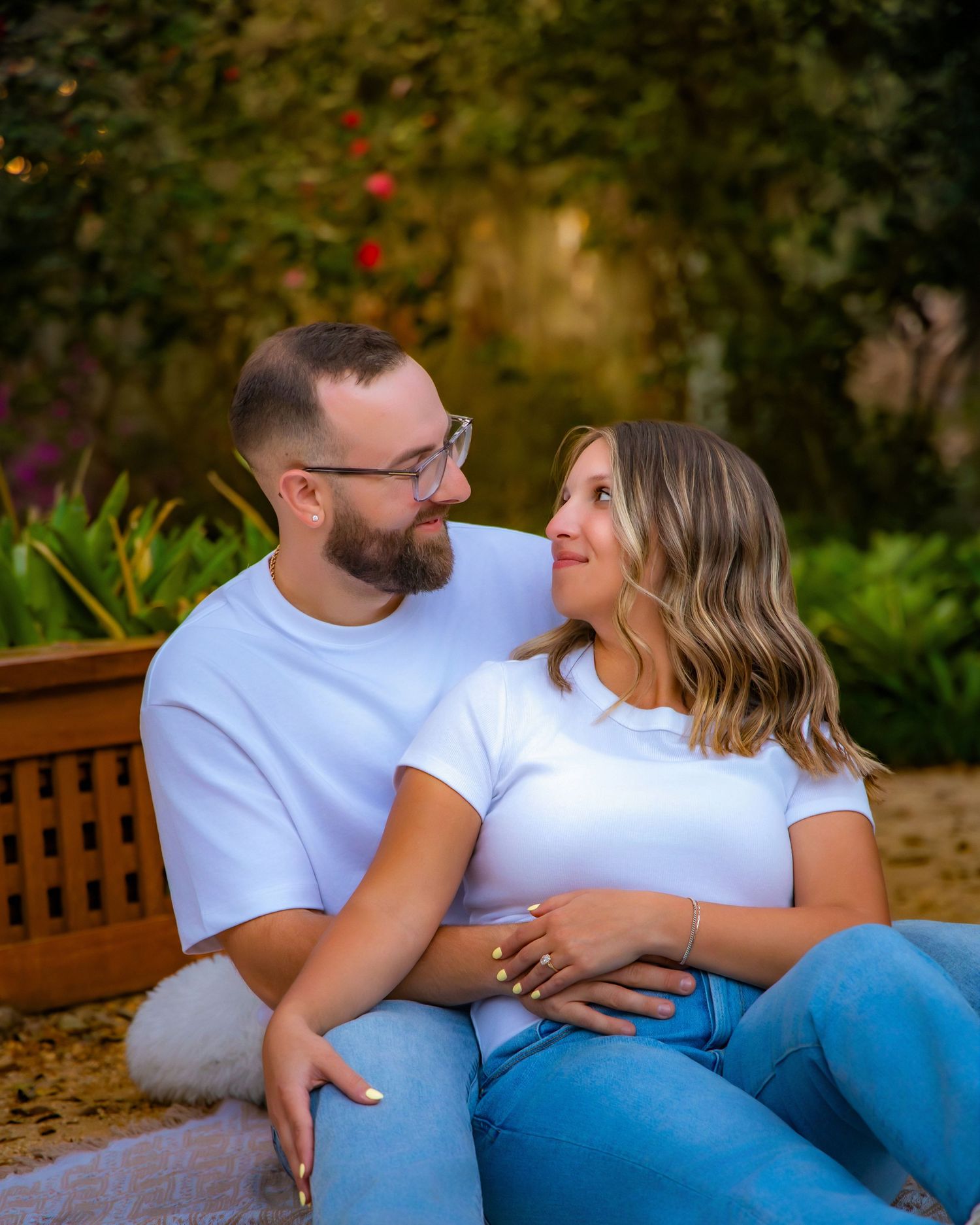 A couple in matching white shirts and jeans laying on grass together during a romantic outdoor photoshoot.