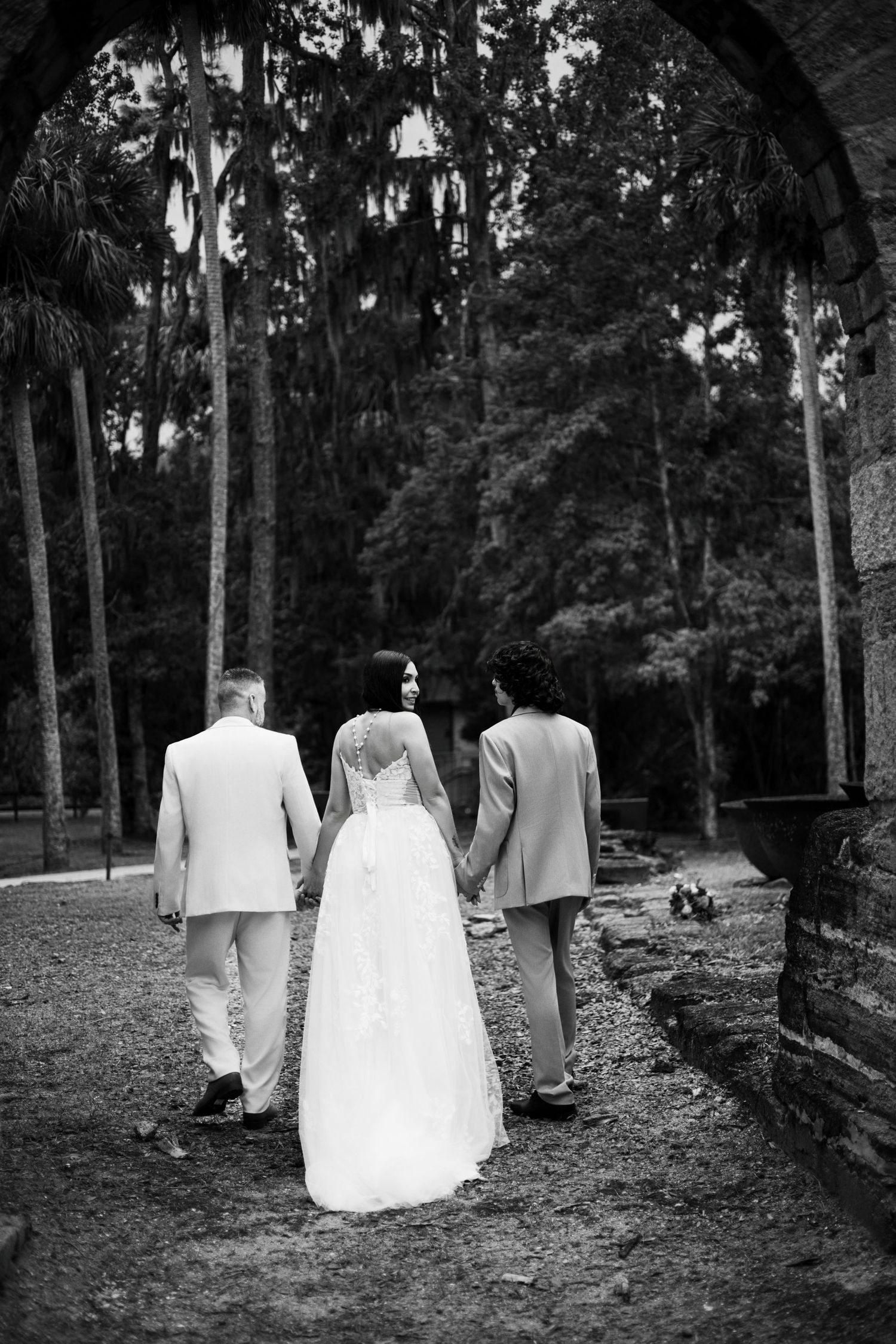 Black and white photo of wedding party walking through tree-lined path.