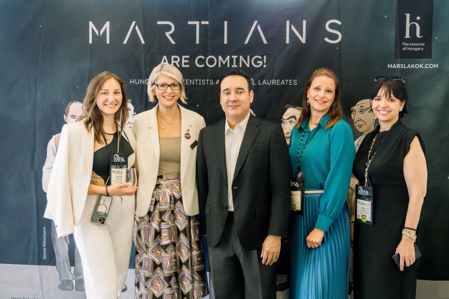 Five professionals posing in front of a Martians Are Coming event backdrop at a conference.
