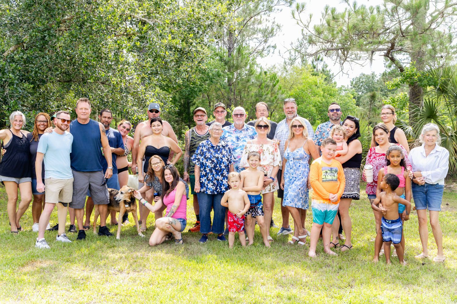 Large family group photo outdoors in a lush green yard, smiling adults and children gathered together for a reunion.