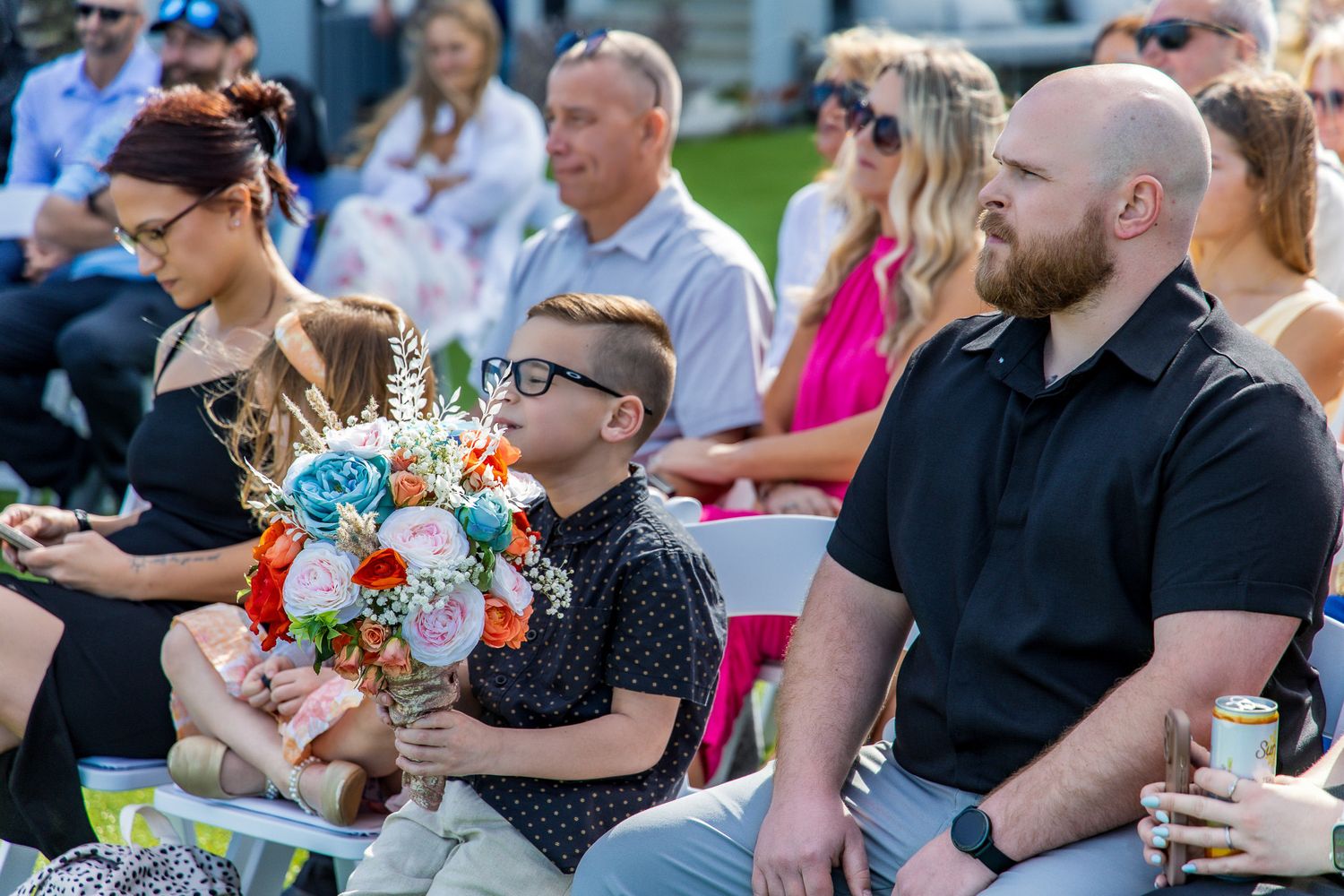 Wedding guests sitting outdoors at a summer celebration with colorful floral centerpieces and decor.