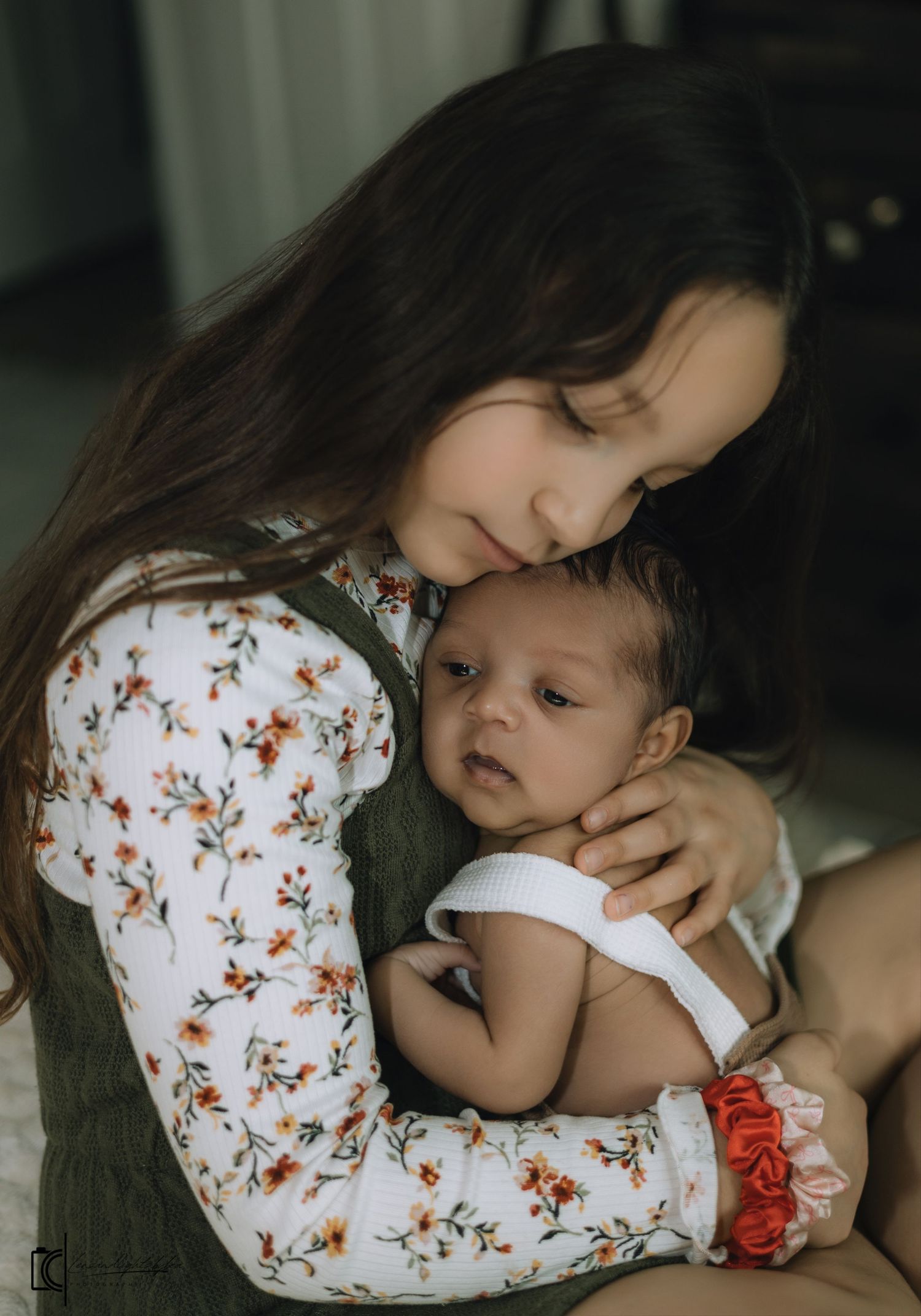 A tender moment between parent and baby wearing a floral print top and white outfit, sharing gentle cuddles.