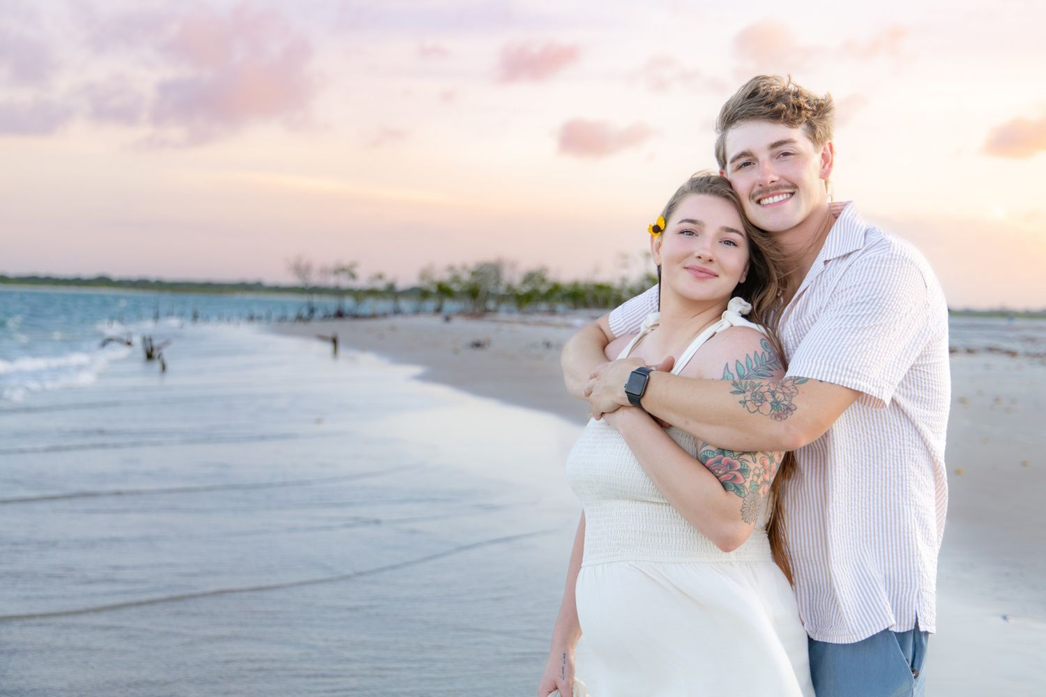 Happy couple embracing on tropical beach at colorful pastel sunset.