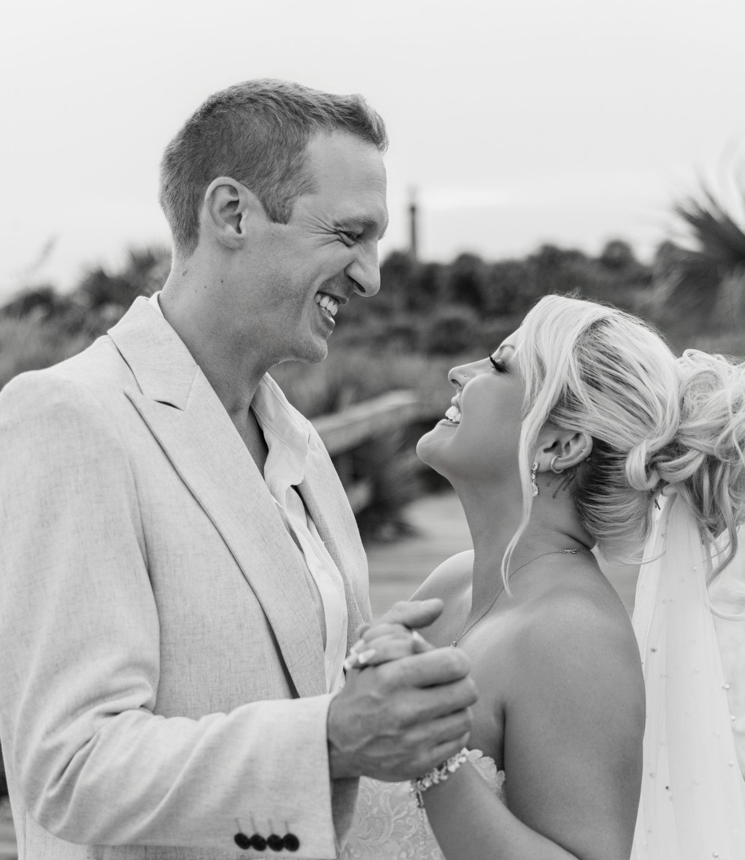 Black and white photo of a smiling bride and groom sharing a joyful moment at an outdoor beach wedding.