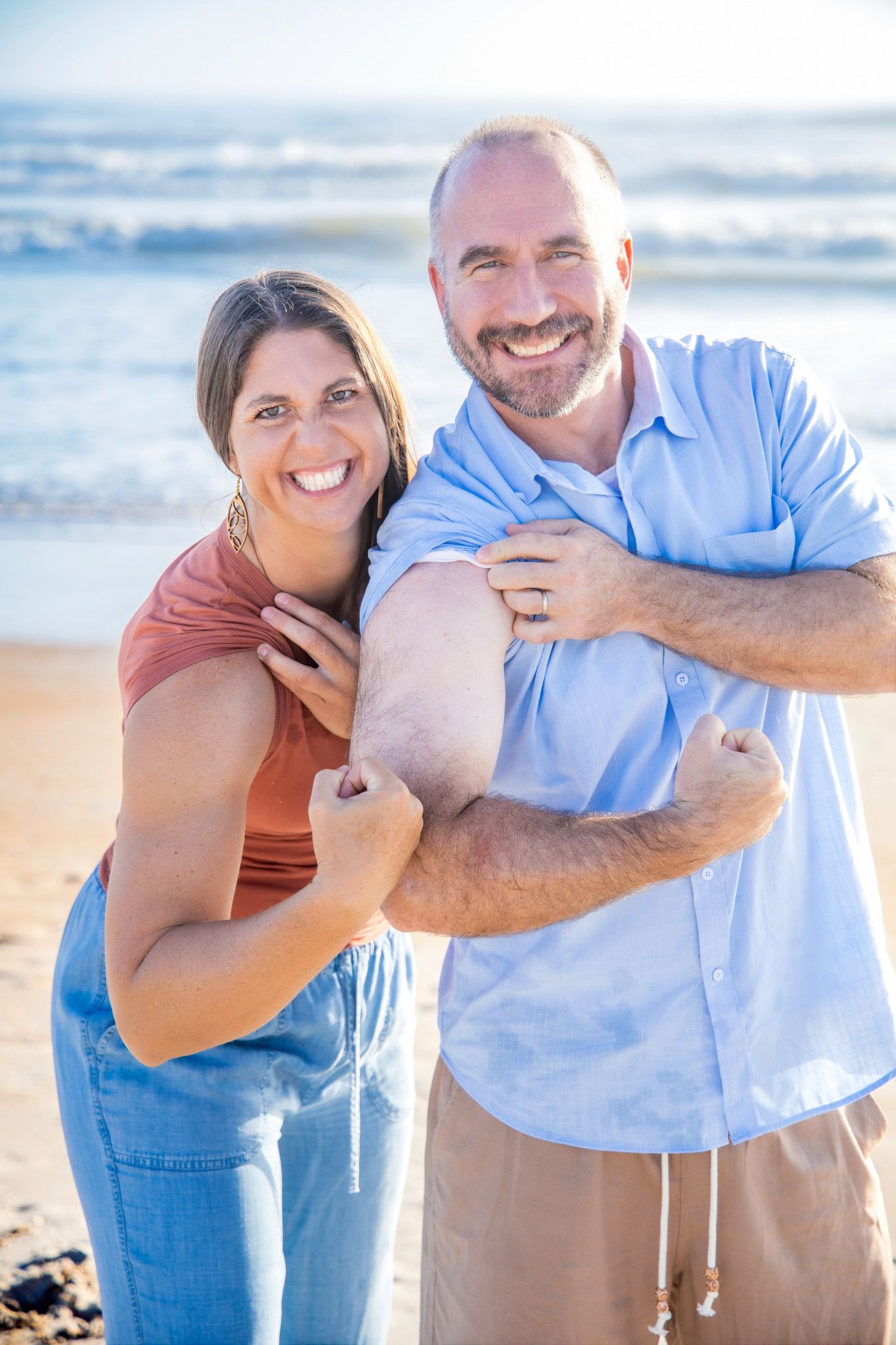 Happy couple embracing and laughing together on sunny beach in casual attire.