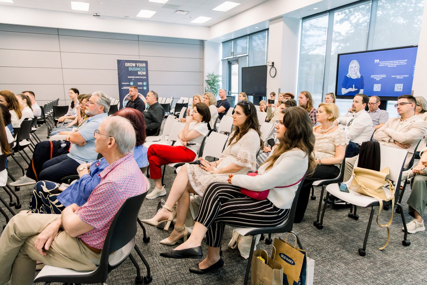 Audience of professionals seated in rows at a corporate conference or business seminar in a modern meeting room.
