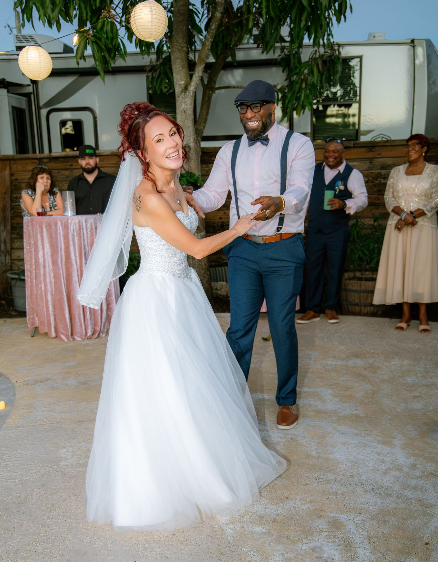 A couple dances together at an outdoor wedding reception venue with paper lantern decorations and guests watching.