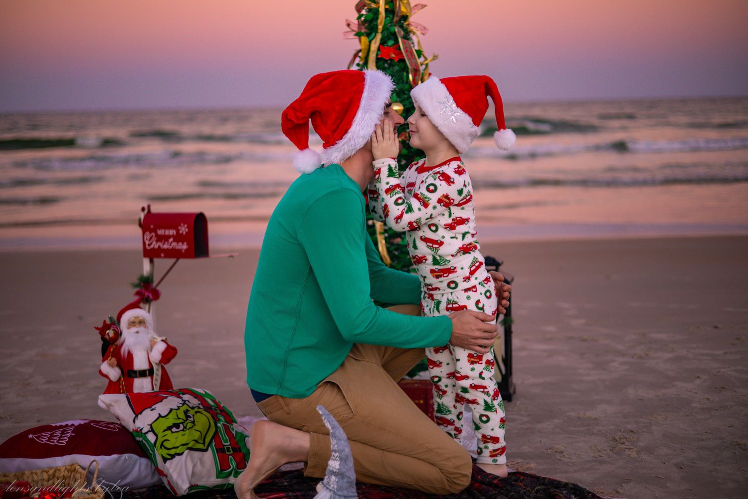 A family in holiday attire takes Christmas photos together on a sandy beach at sunset.