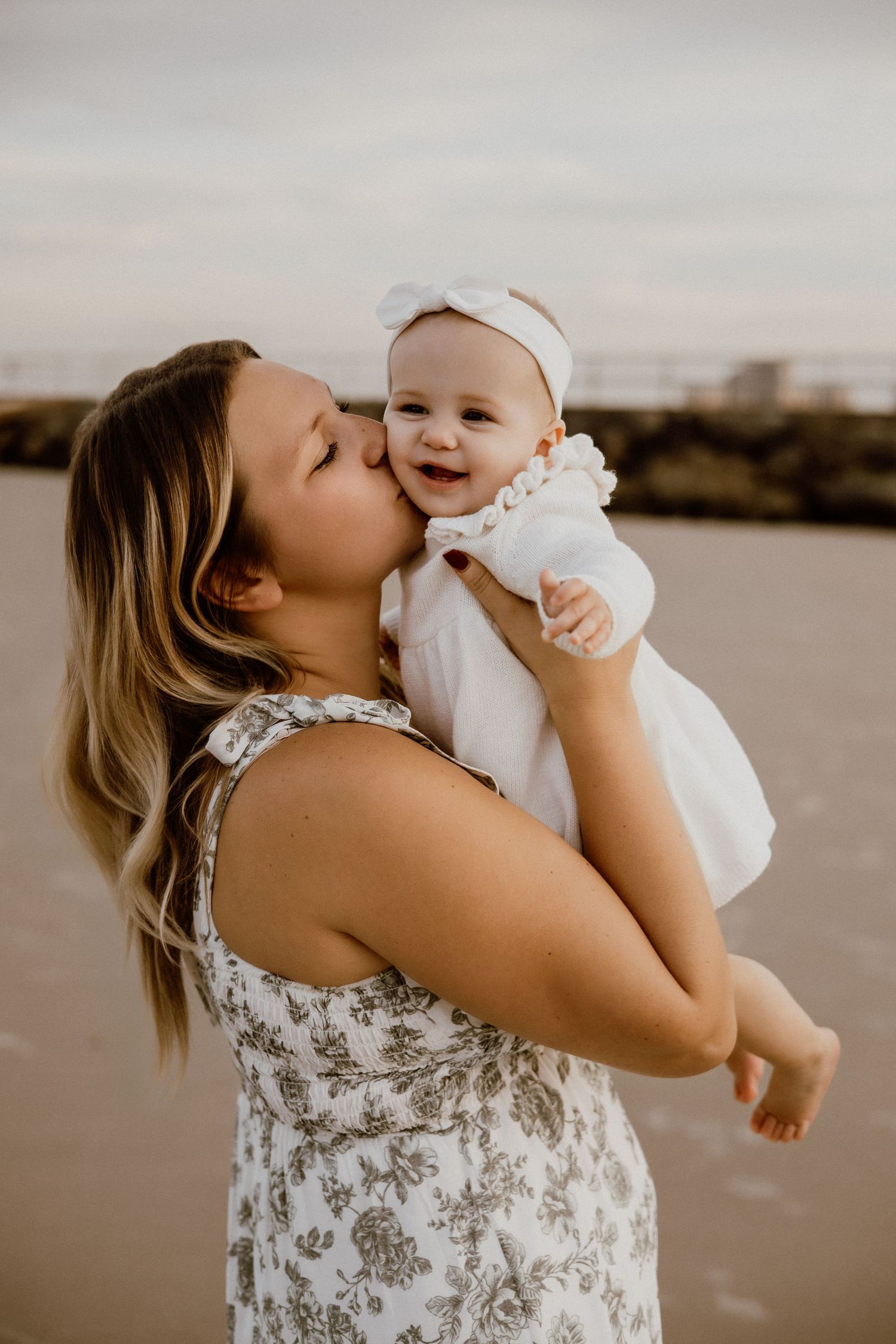 Mother and baby sharing joyful moments on a beach at sunset.
