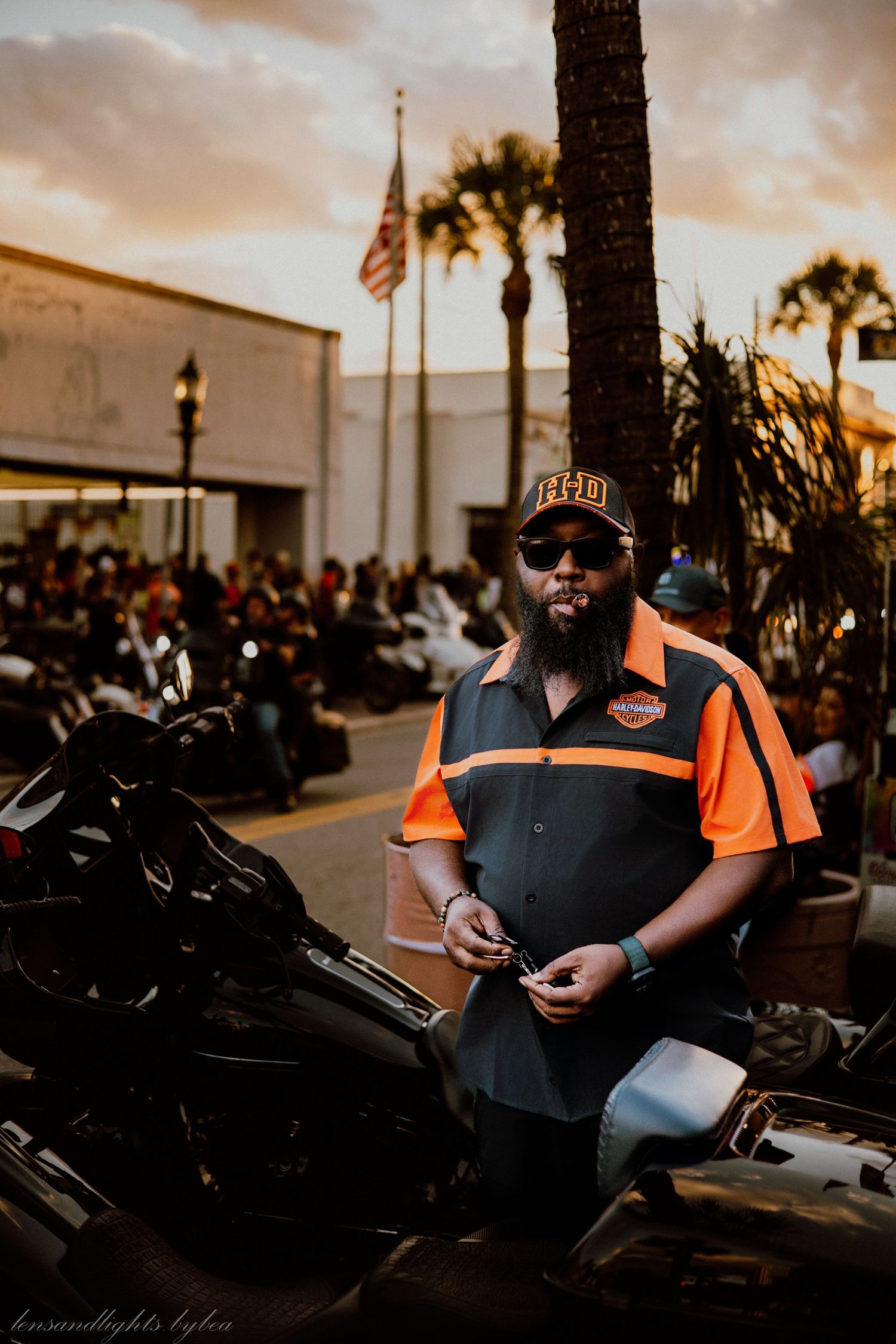 A person in black and orange sits on a motorcycle at sunset during a gathering of bikers.