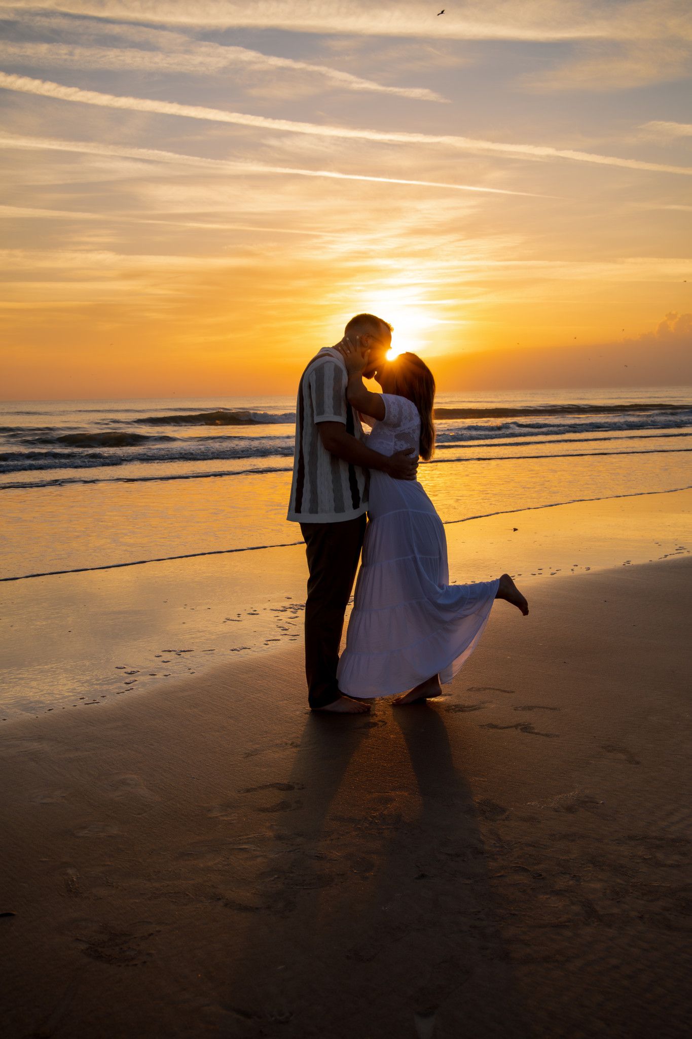 A silhouetted couple embraces on a beach at sunset with golden light reflecting off the ocean waves.