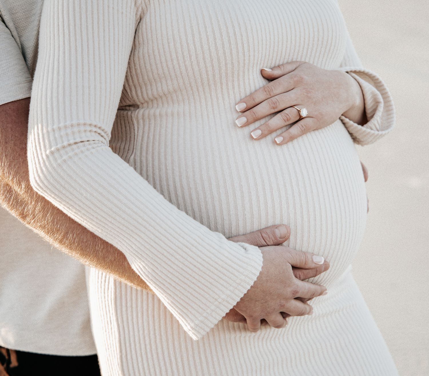 Close up series of hands gently cradling a pregnant belly in a white ribbed sweater.