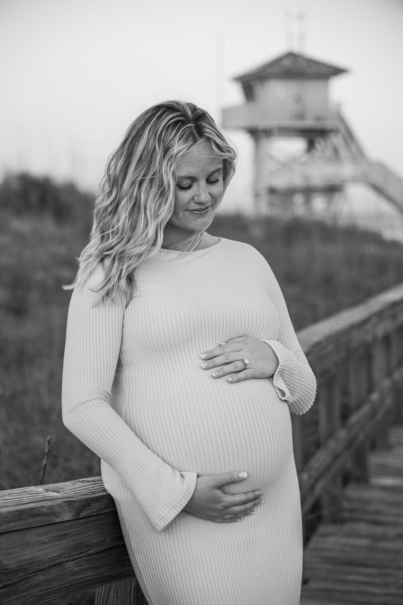 A series of black and white maternity photos showing an expectant mother in a white sweater on a wooden boardwalk.