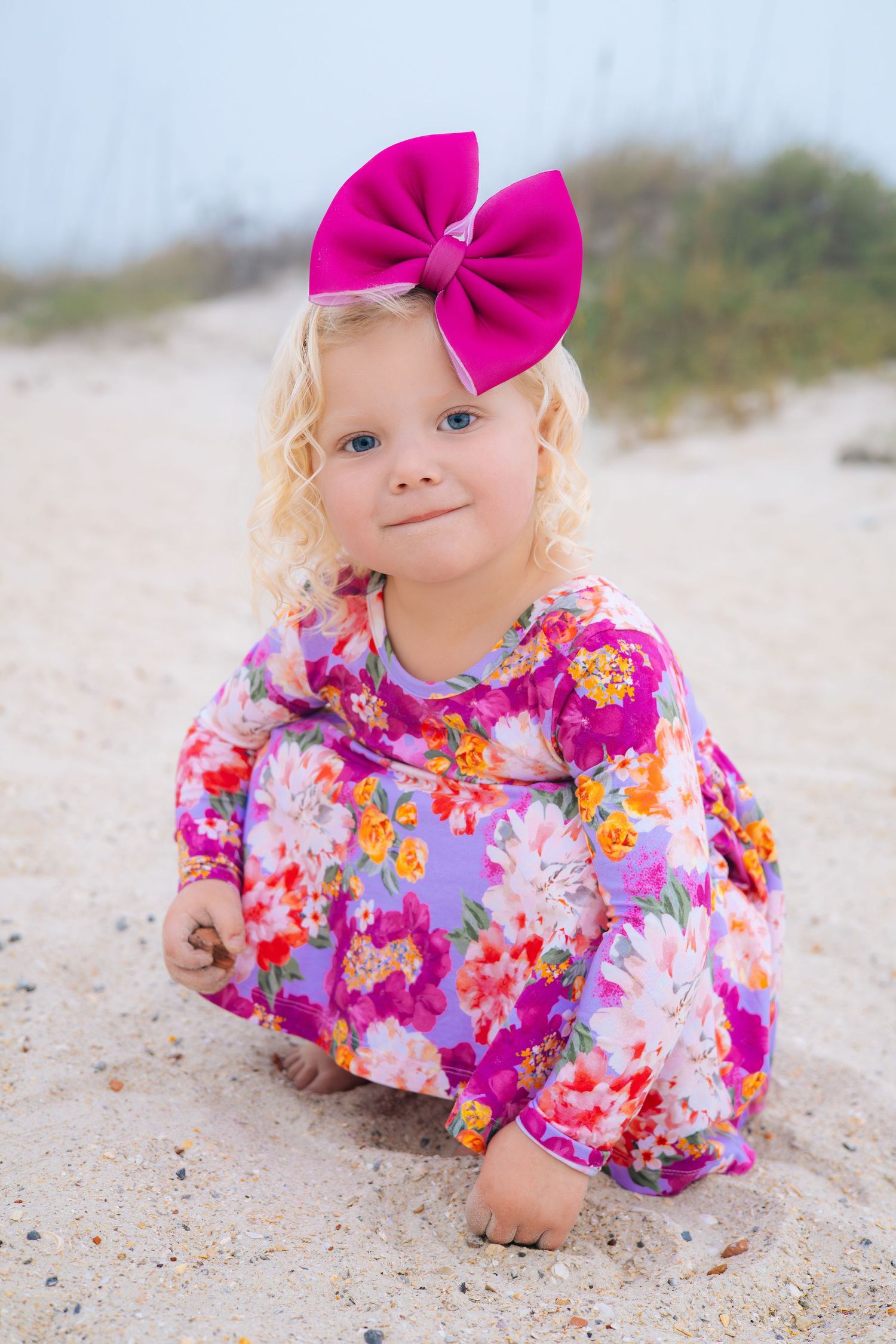 Series of photos showing a young child in a pink floral dress and bow lying on sandy beach.
