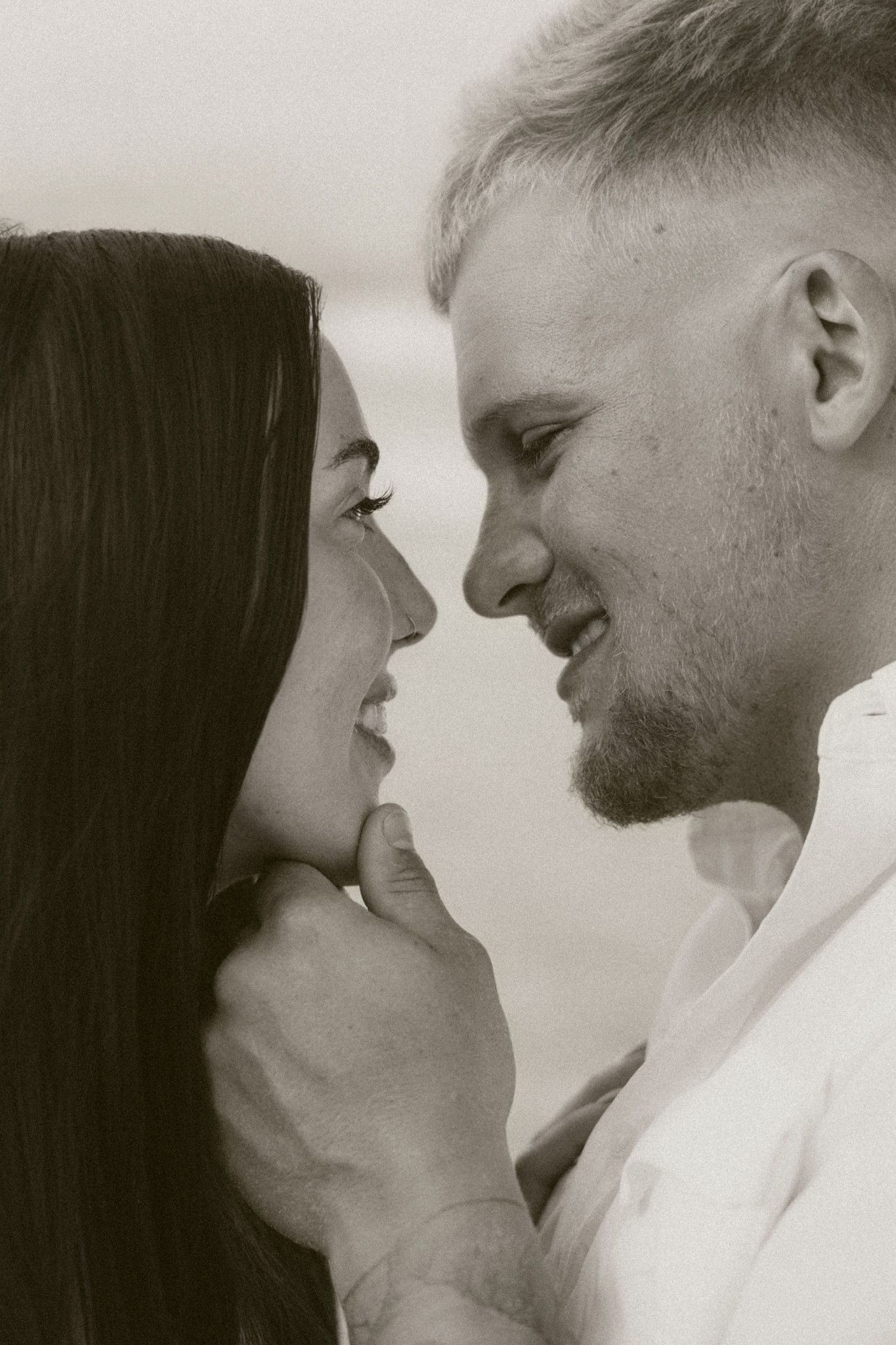 Black and white photo of a smiling couple gazing at each other tenderly, man gently holding womans chin.
