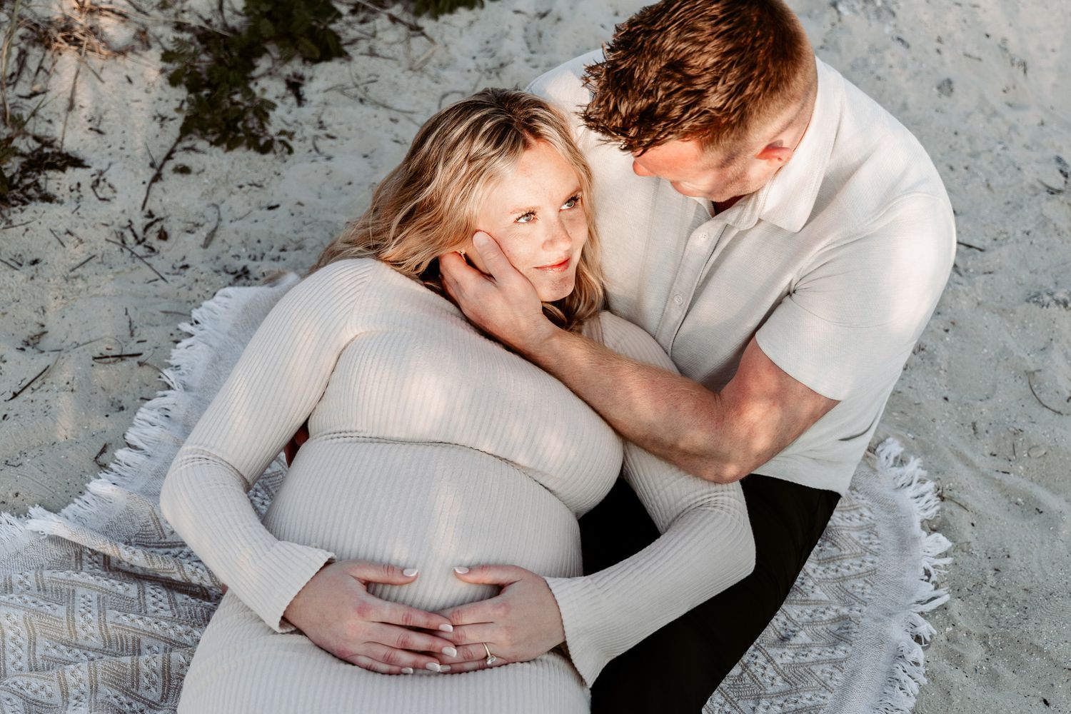 Intimate maternity photo series showing couple in white outfits on gray textured backdrop.