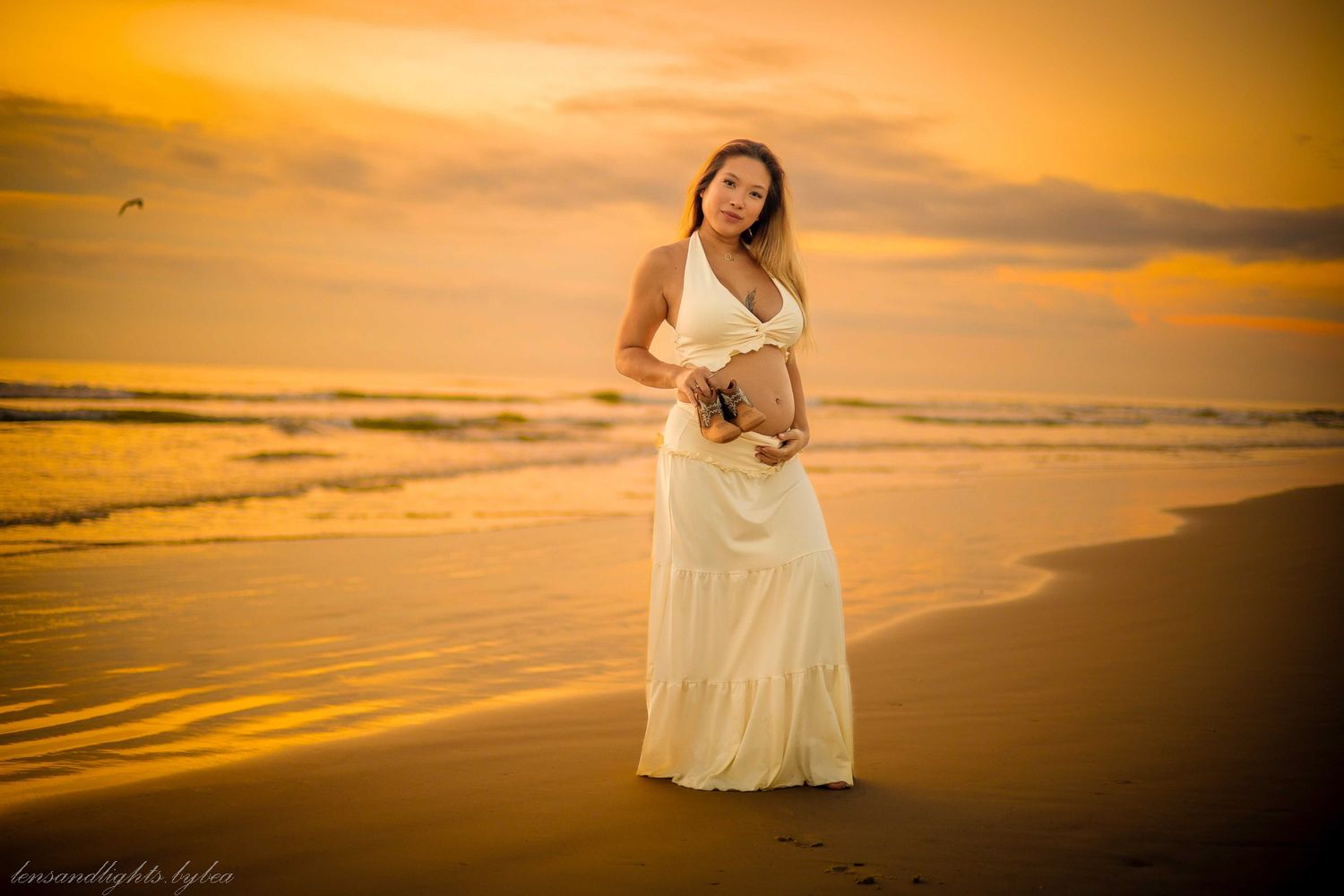 Woman in white dress walking along beach at golden sunset.