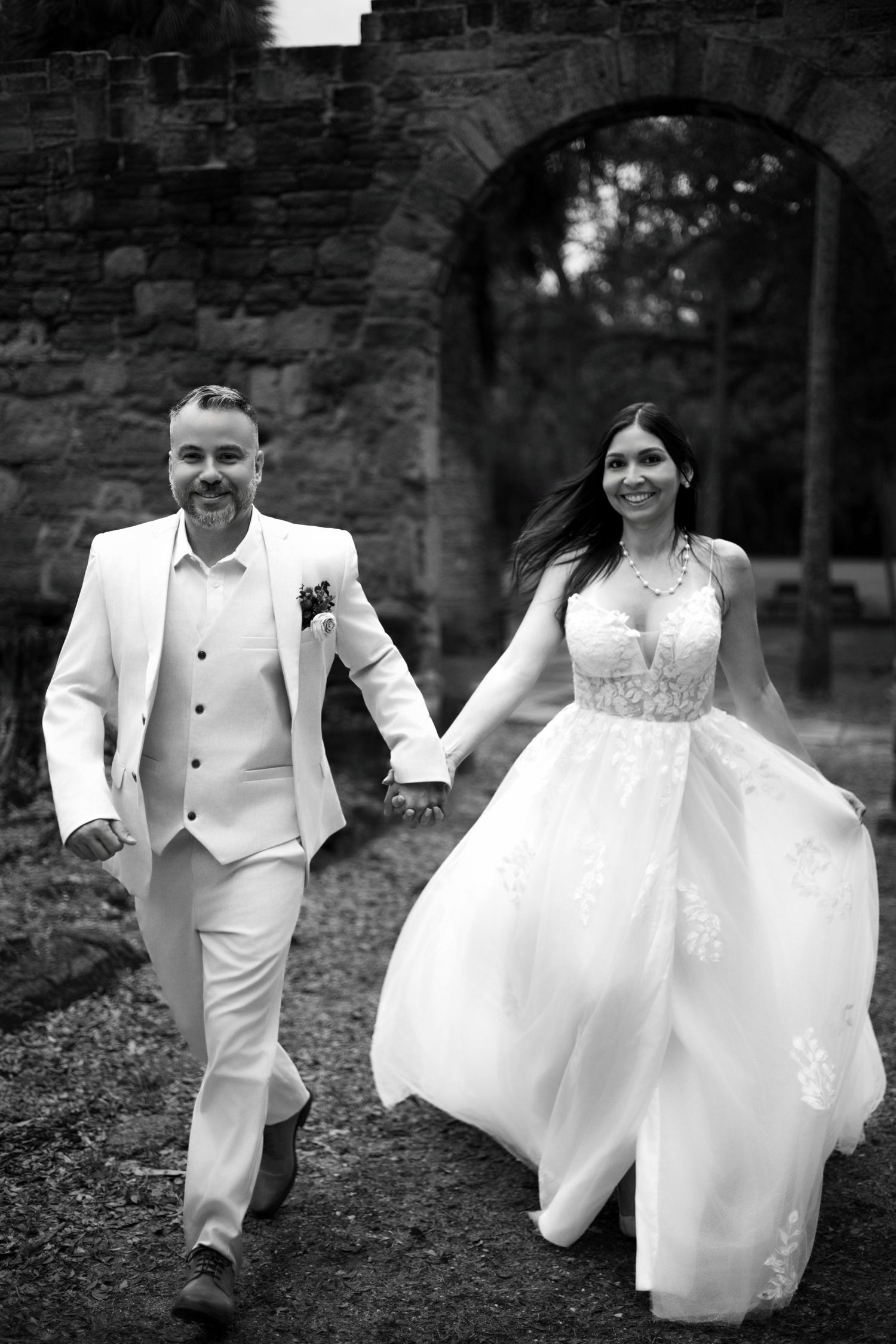 Black and white wedding photos showing a couple in white attire walking and posing together outdoors.