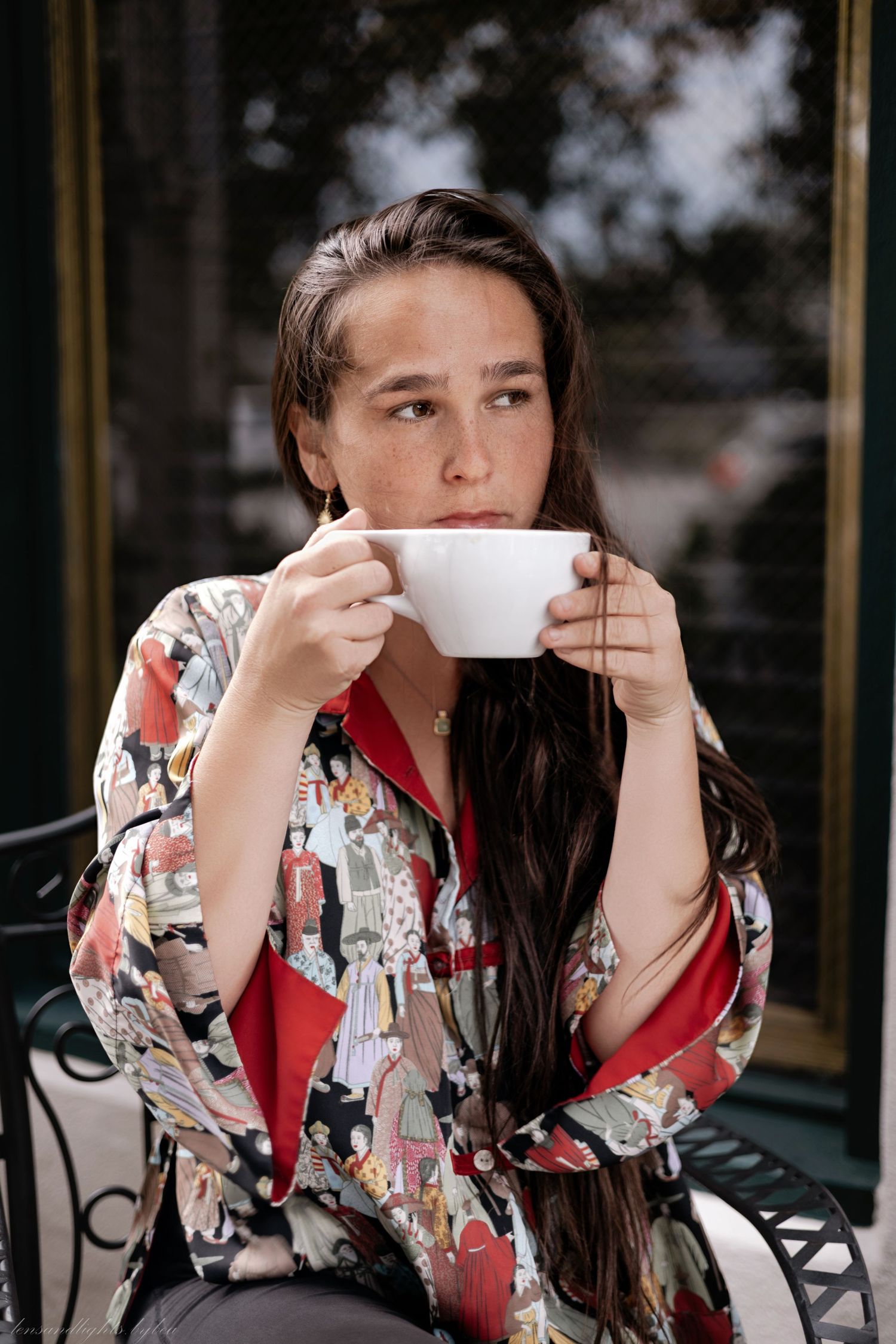 Person in floral kimono drinking from white teacup in cafe setting.