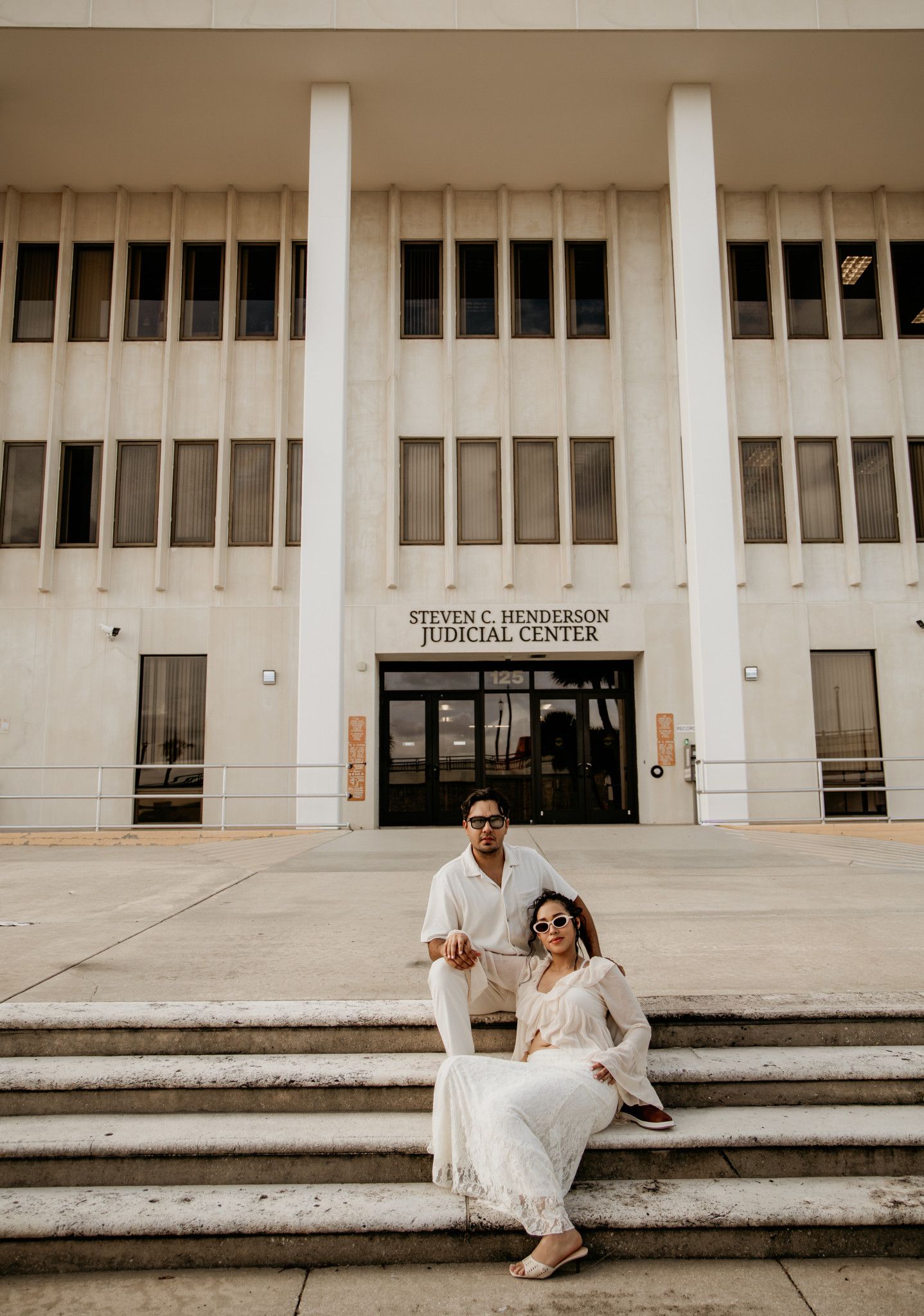 Couple in white attire posing on steps of Steven C. Henderson Judicial Center for wedding photos.