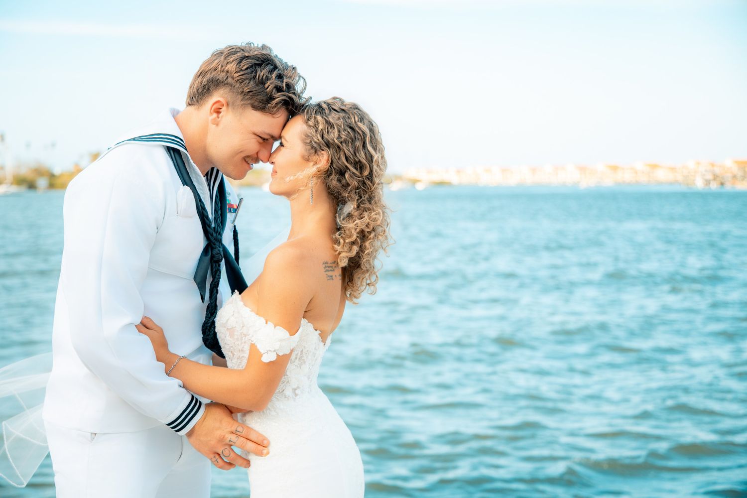 A sailor in white uniform and a woman in a white dress share a romantic moment by the ocean.