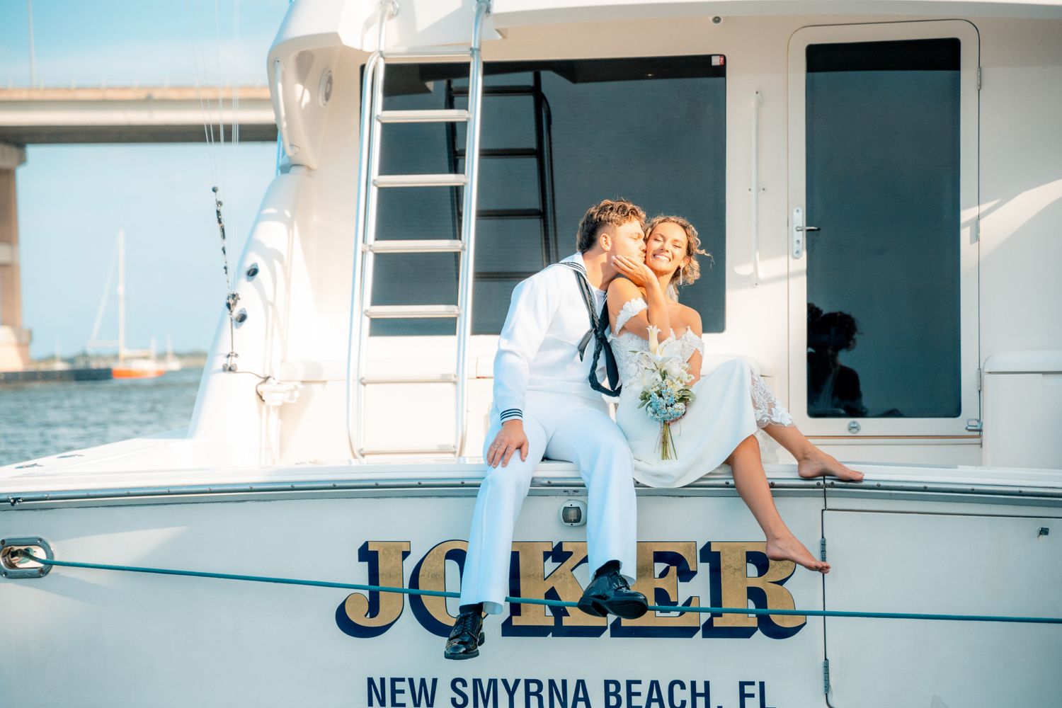 Couple in wedding attire sitting on the stern of a yacht named Joker in New Smyrna Beach, FL.