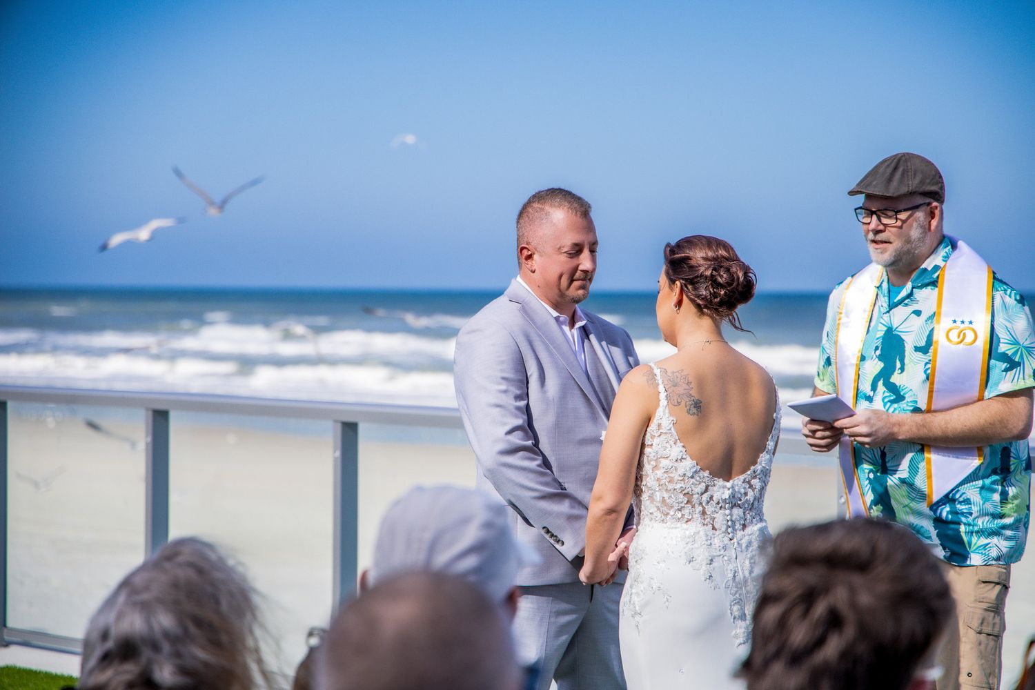 A group of people gather on a beach for a casual outdoor celebration with seagulls flying overhead.