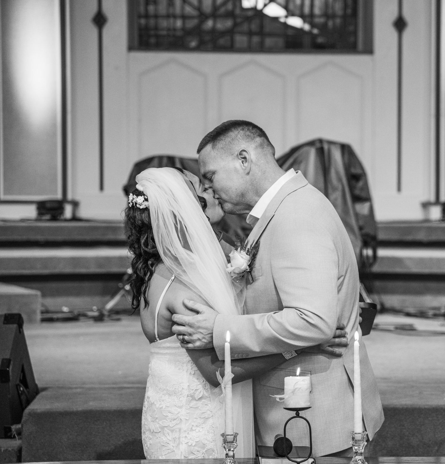 Black and white photo of a bride and groom sharing their first kiss at the altar during a church wedding ceremony.