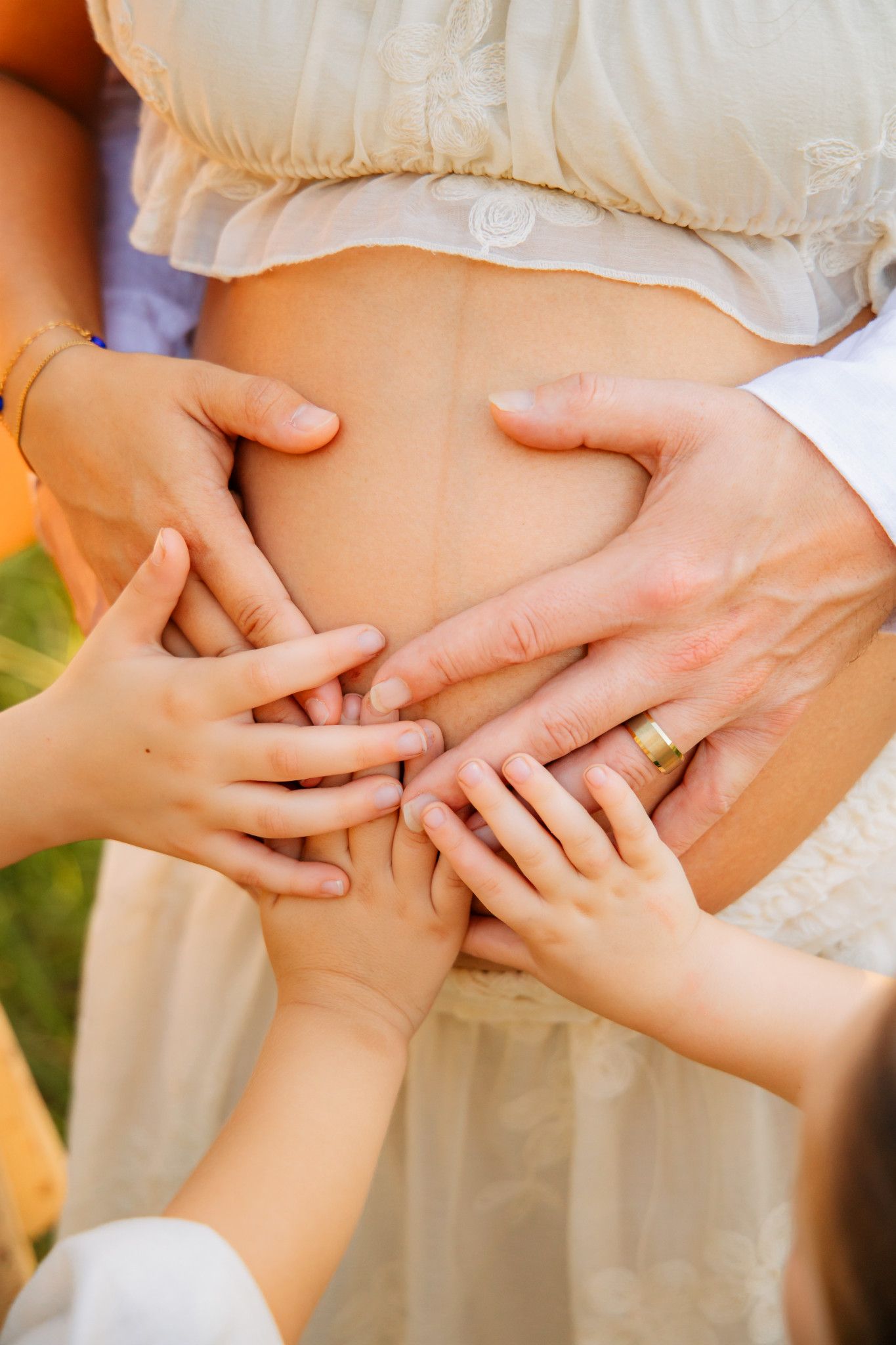 Family hands touching pregnant woman's bare belly outdoors, symbolizing love and anticipation for new baby.